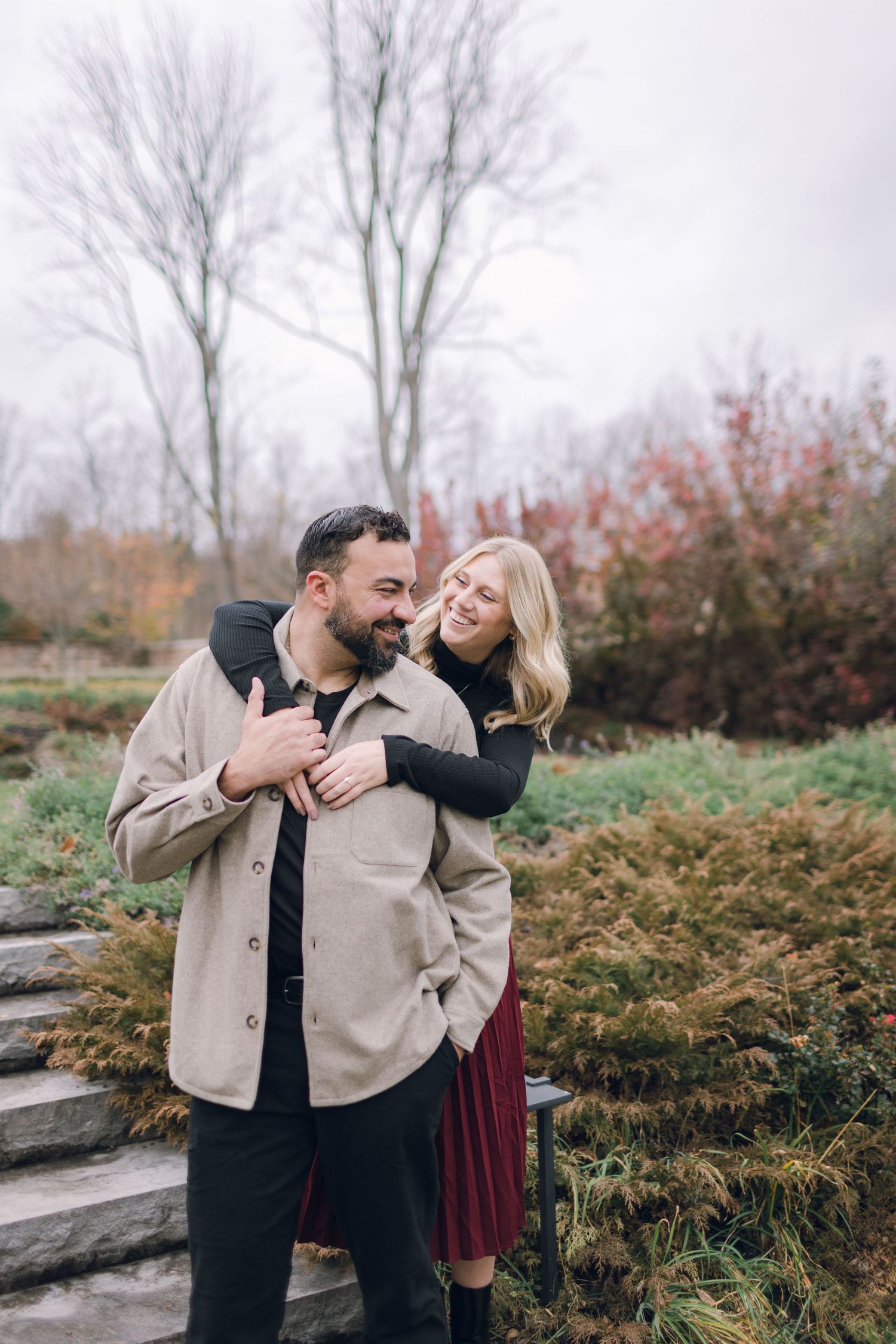 Couple shares a romantic autumn moment outdoors among bare trees and fall foliage.