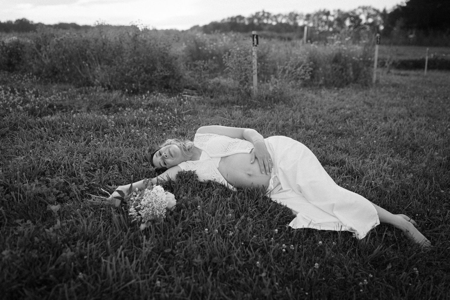 A person in a white dress lies peacefully in a grassy meadow on a sunny day.