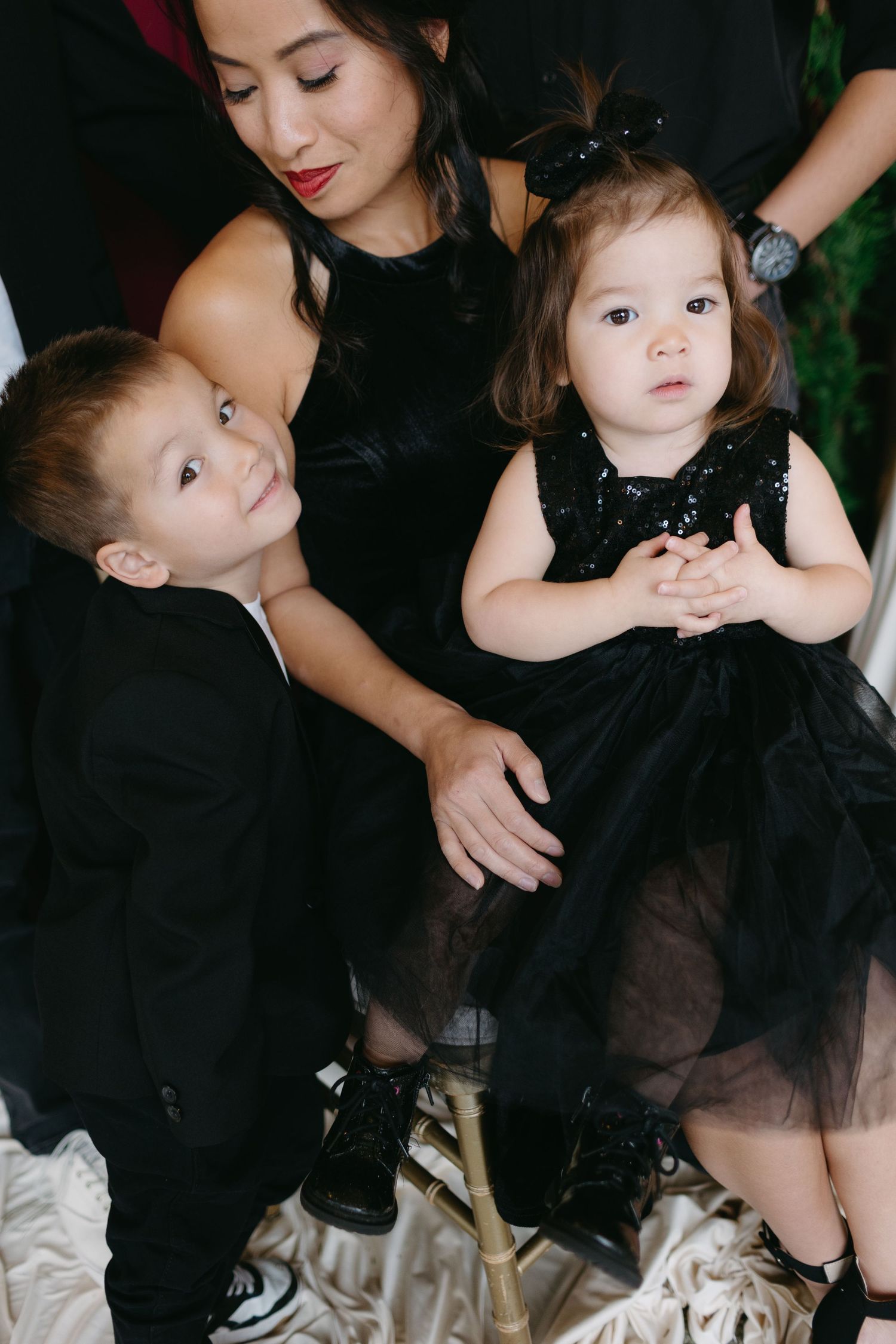 Two children in black formal attire sitting together on white fabric.
