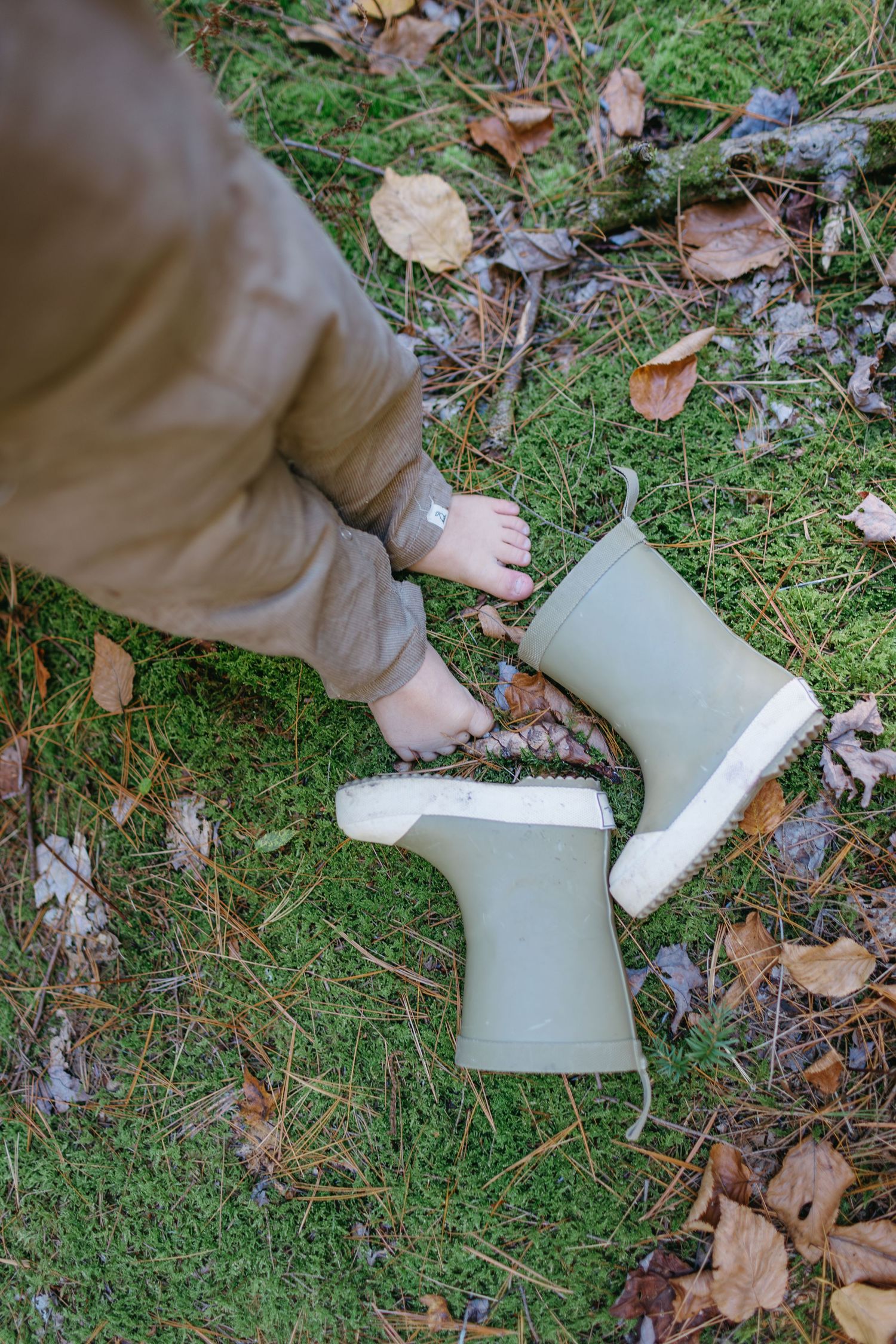 Small beige winter boots on grass covered with fallen autumn leaves.