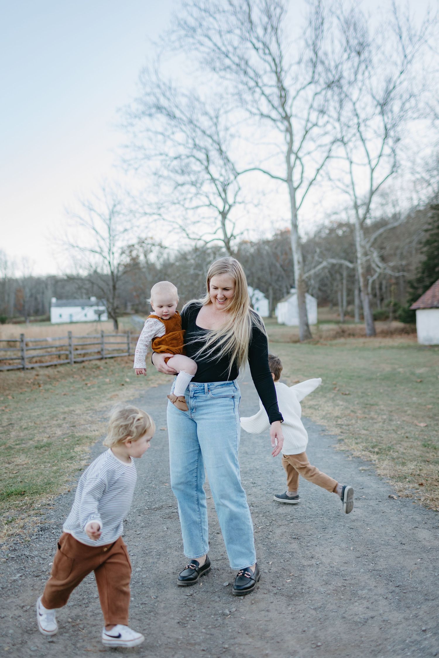 A family walking together on a dirt path with bare trees and farm buildings in the background.