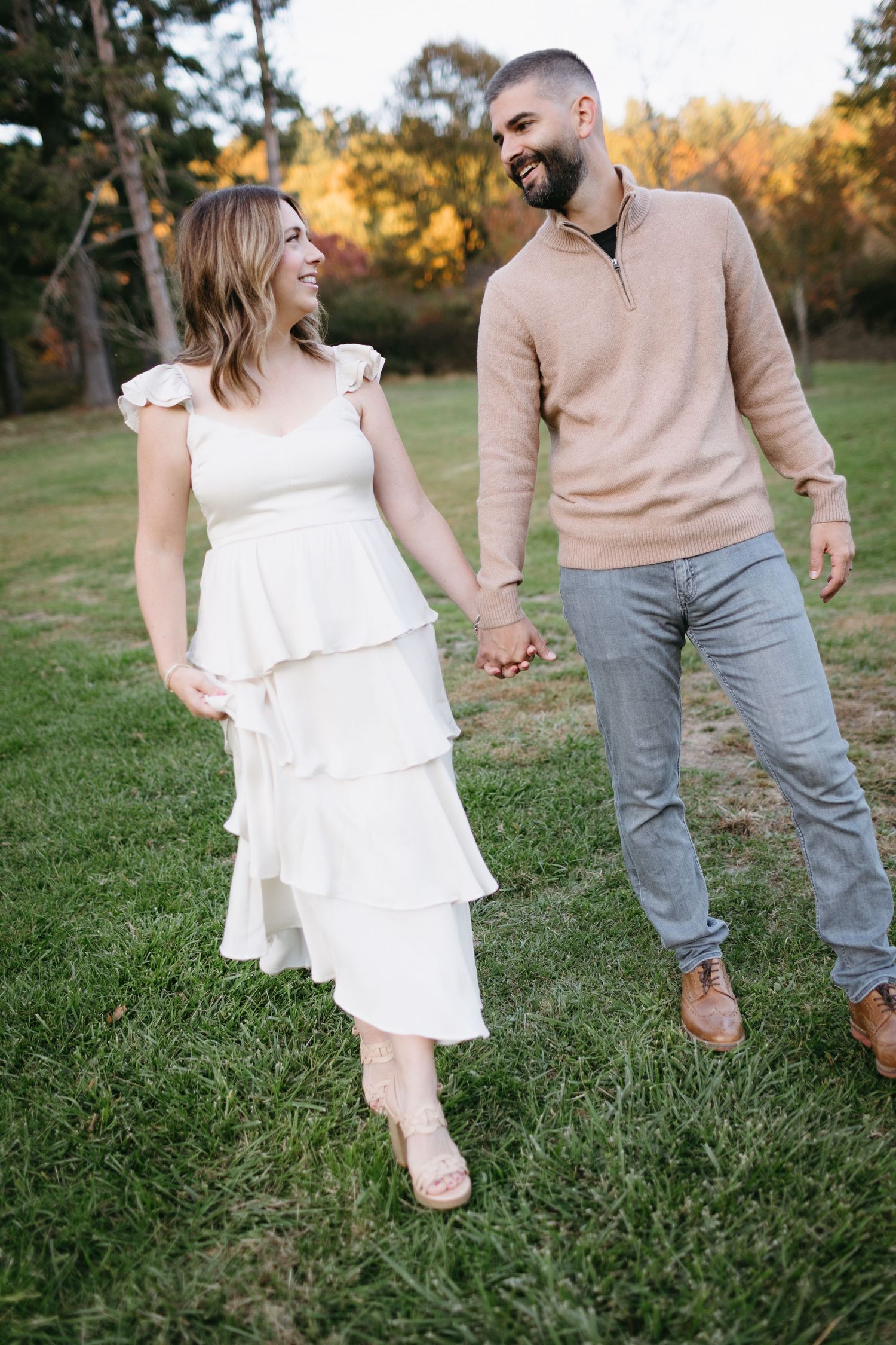 A couple sharing a joyful moment while walking on grass during golden hour.
