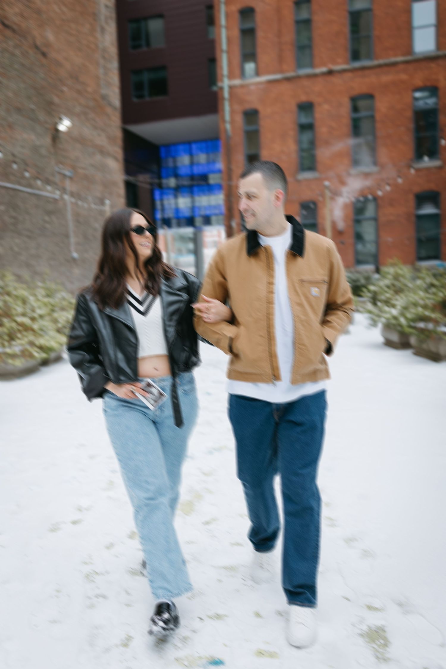 A couple in casual winter attire walking together along a snow-covered city path.
