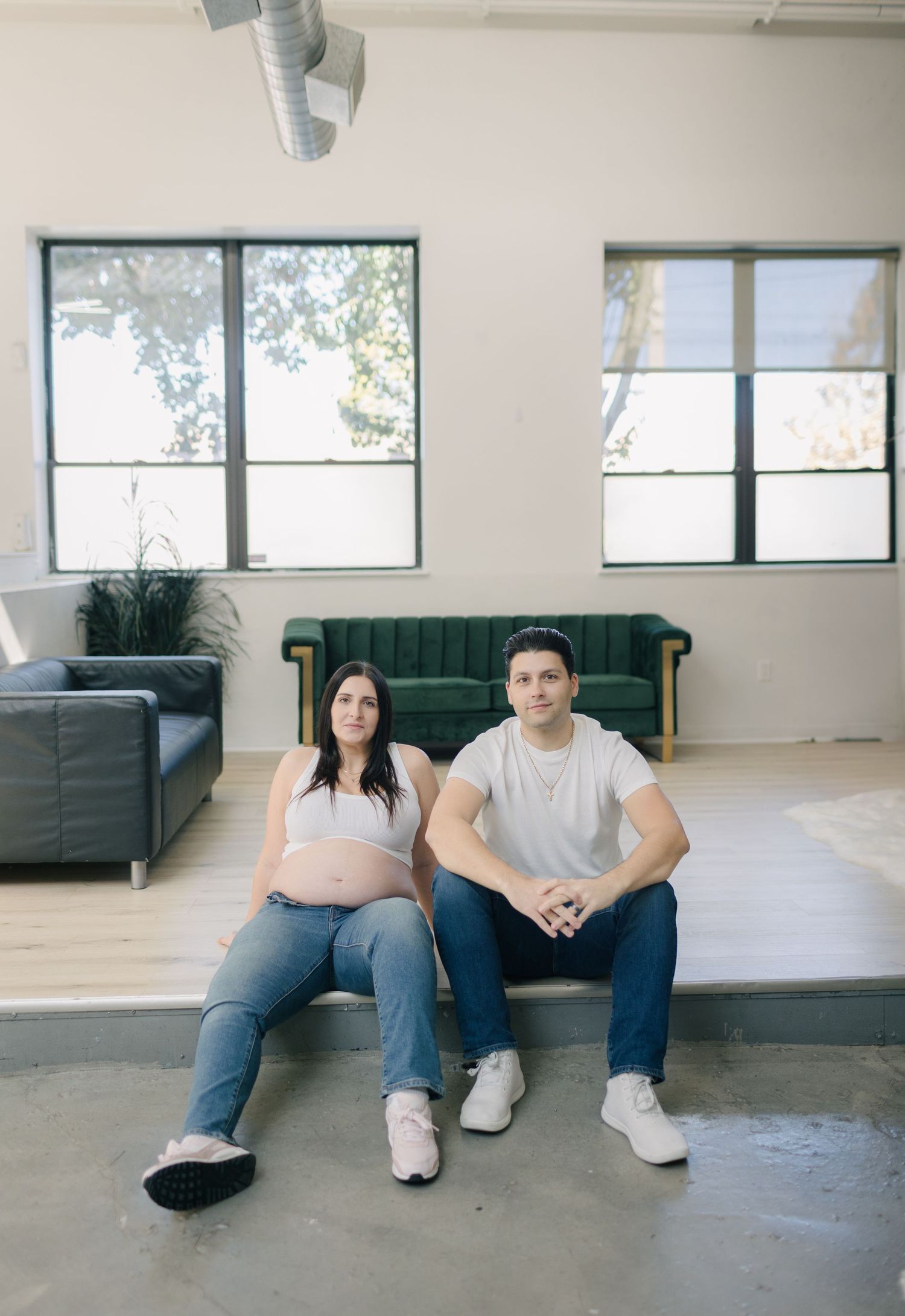 Couple sitting together on green couch in modern minimalist room with large windows.