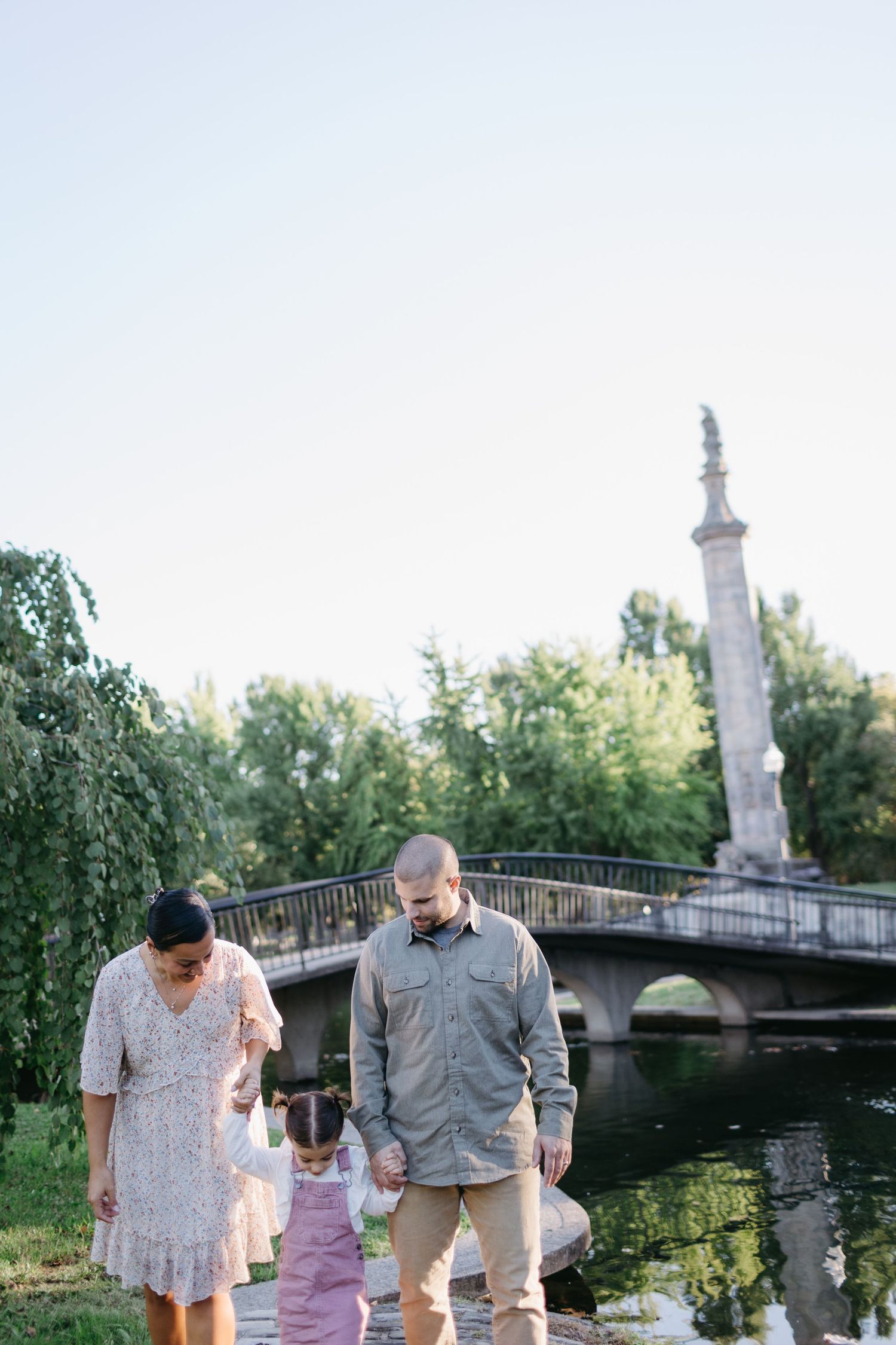 A family enjoying a stroll together by a scenic stone bridge in a park.