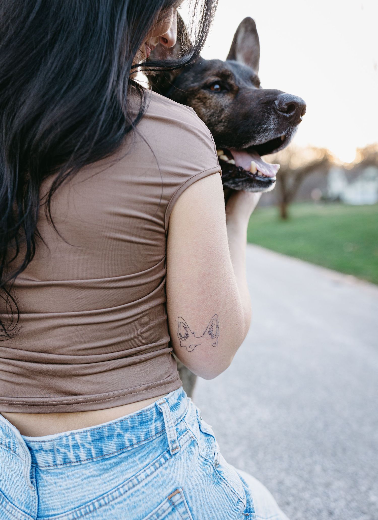 Close up view of woman with German Shepherd showing butterfly tattoo on arm.