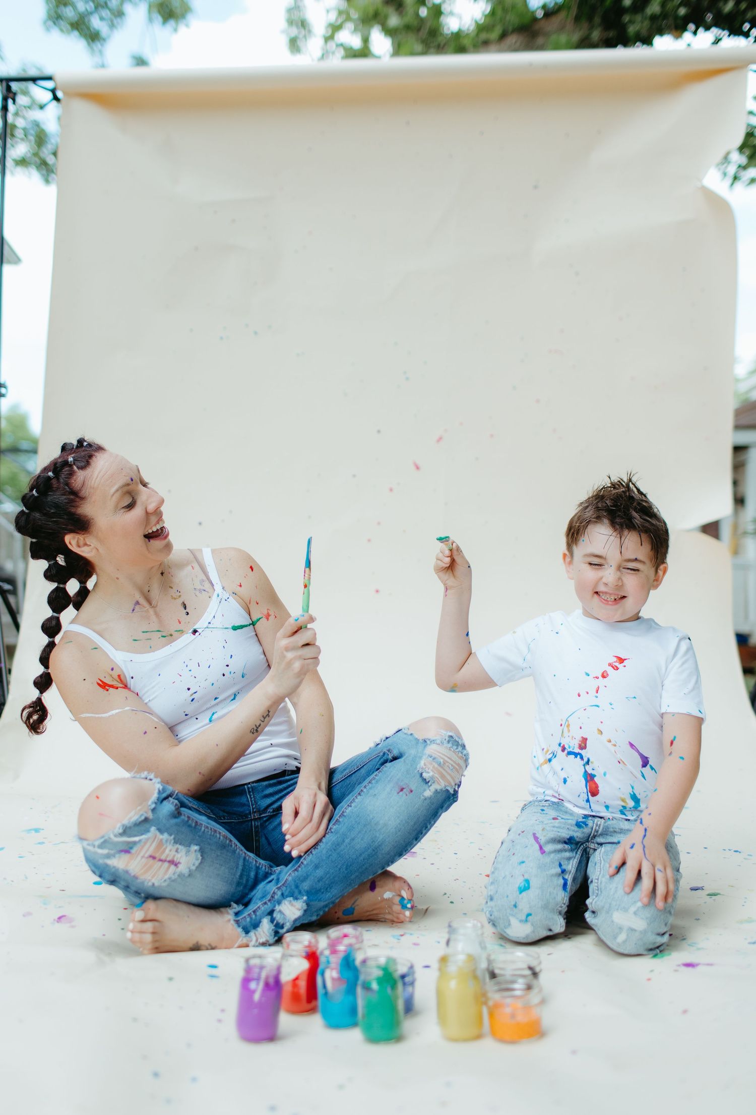Joyful paint play session with colorful bottles on a white backdrop outdoors.