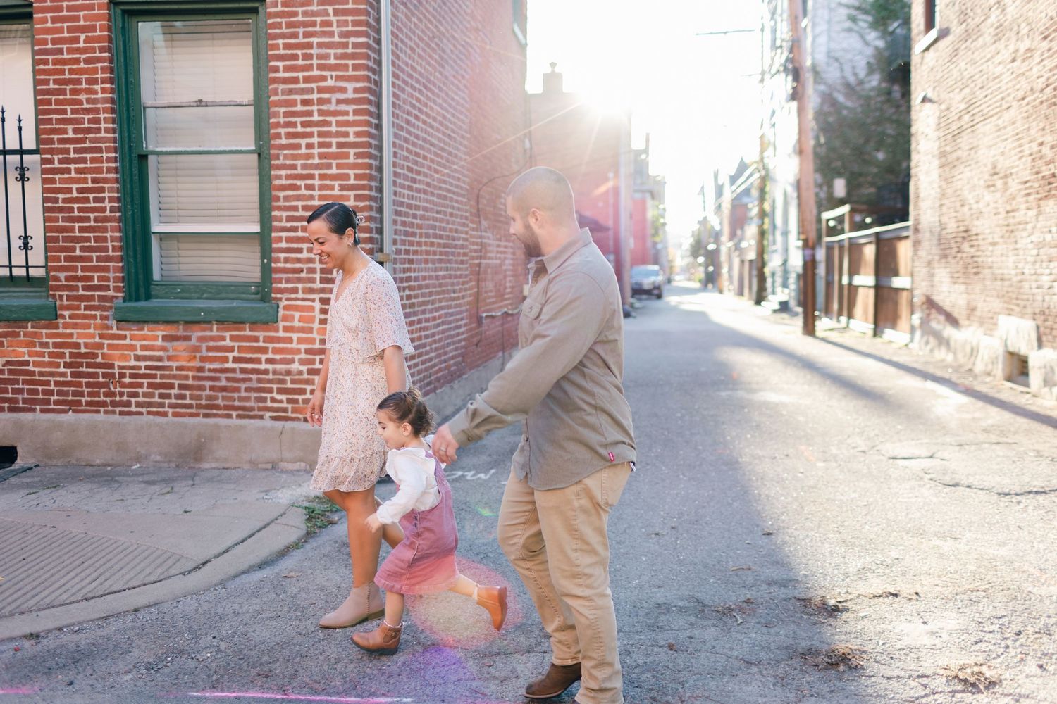 Family walking together on sunny brick-lined street corner in urban setting.