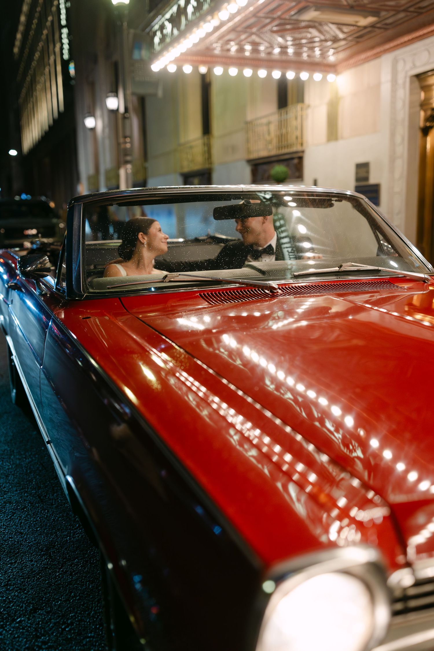 A classic red convertible parked at night under marquee lighting.