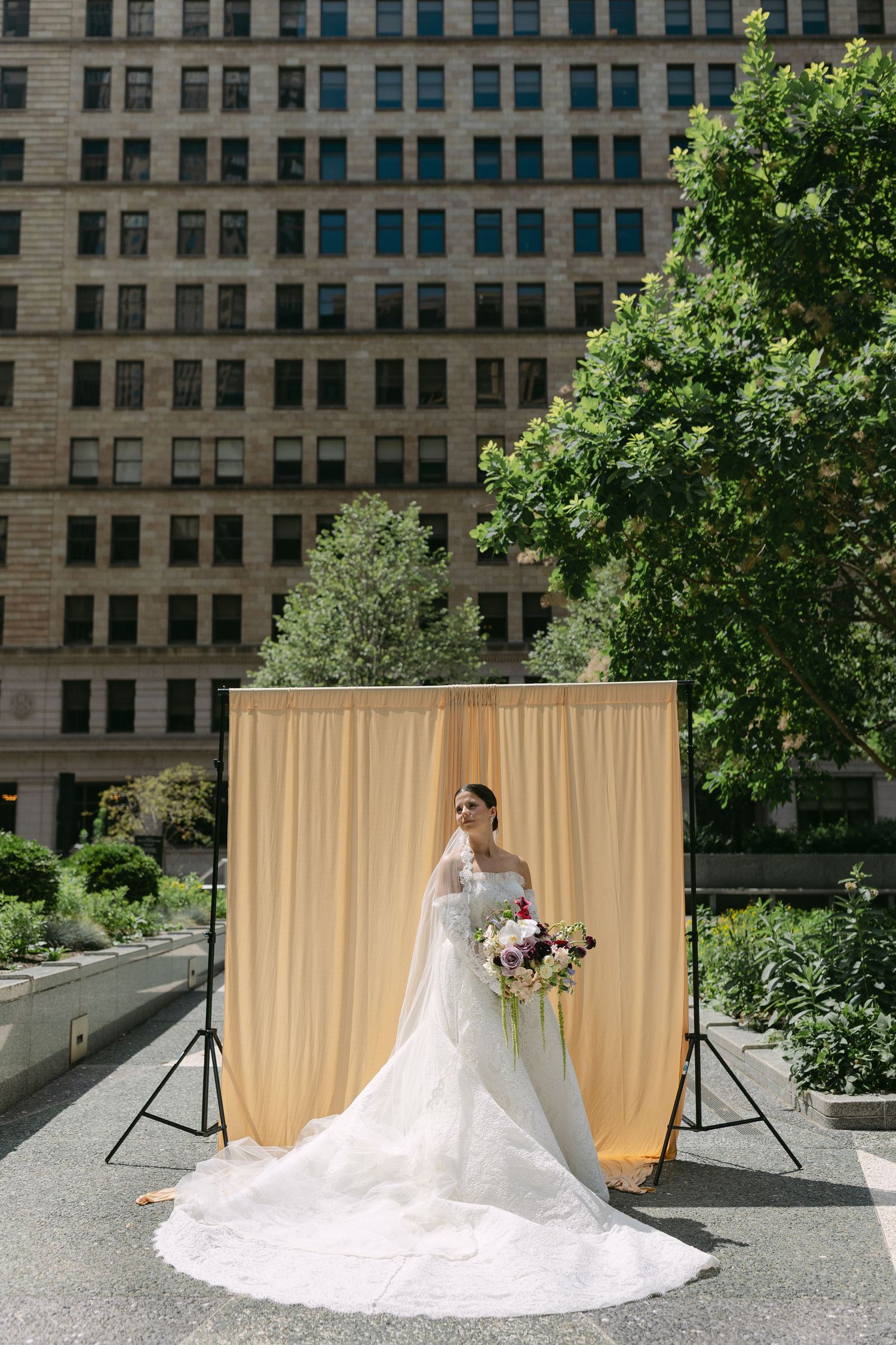 A bridal portrait session outdoors with a beige backdrop and urban architecture in the background.