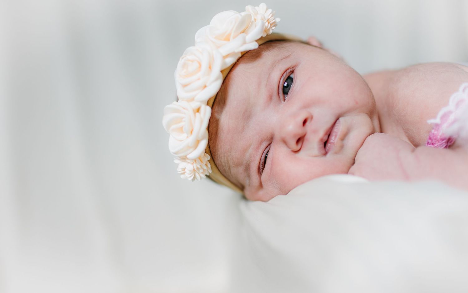 Baby wearing delicate flower crown headband against soft white background.