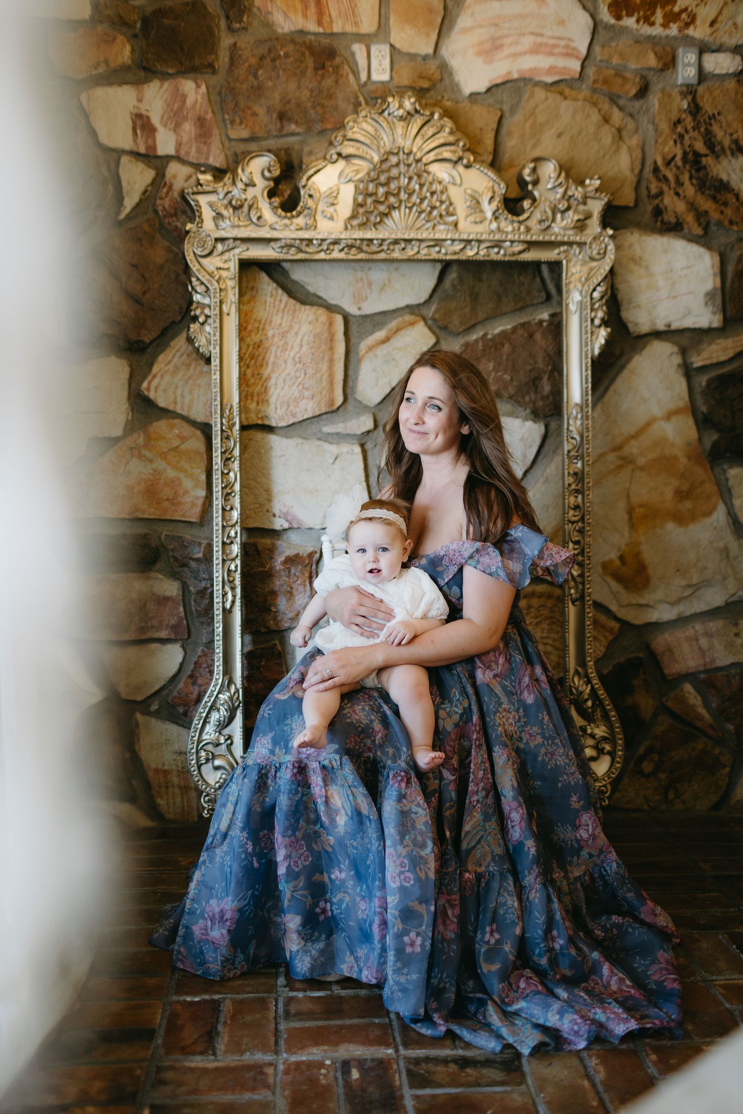 Elegant portrait in ornate gold frame against stone wall backdrop.