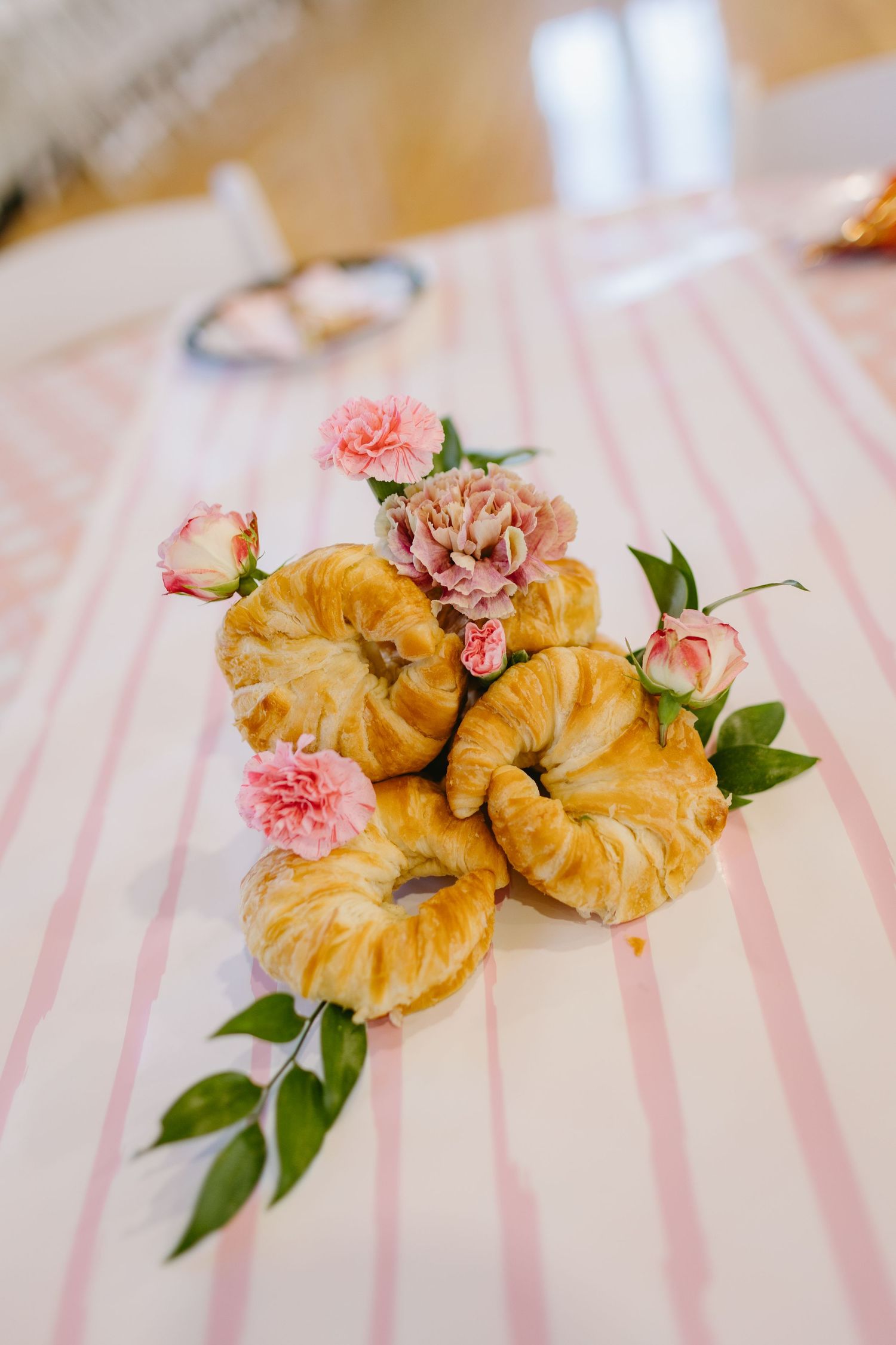 Croissants decorated with pink flowers and greenery on a striped pink tablecloth.