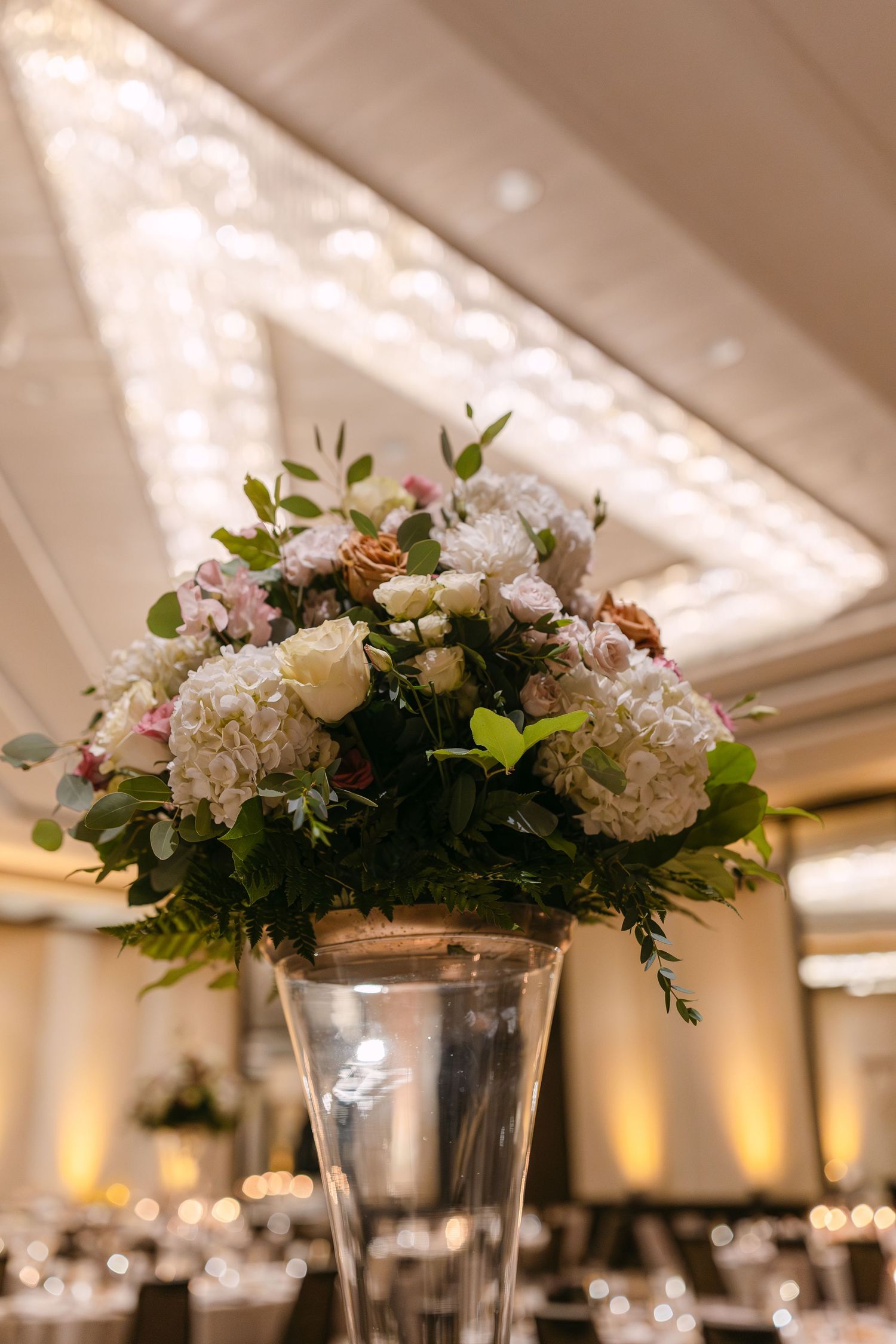 Elegant white and pink floral centerpieces in tall glass vases arranged for a wedding reception.