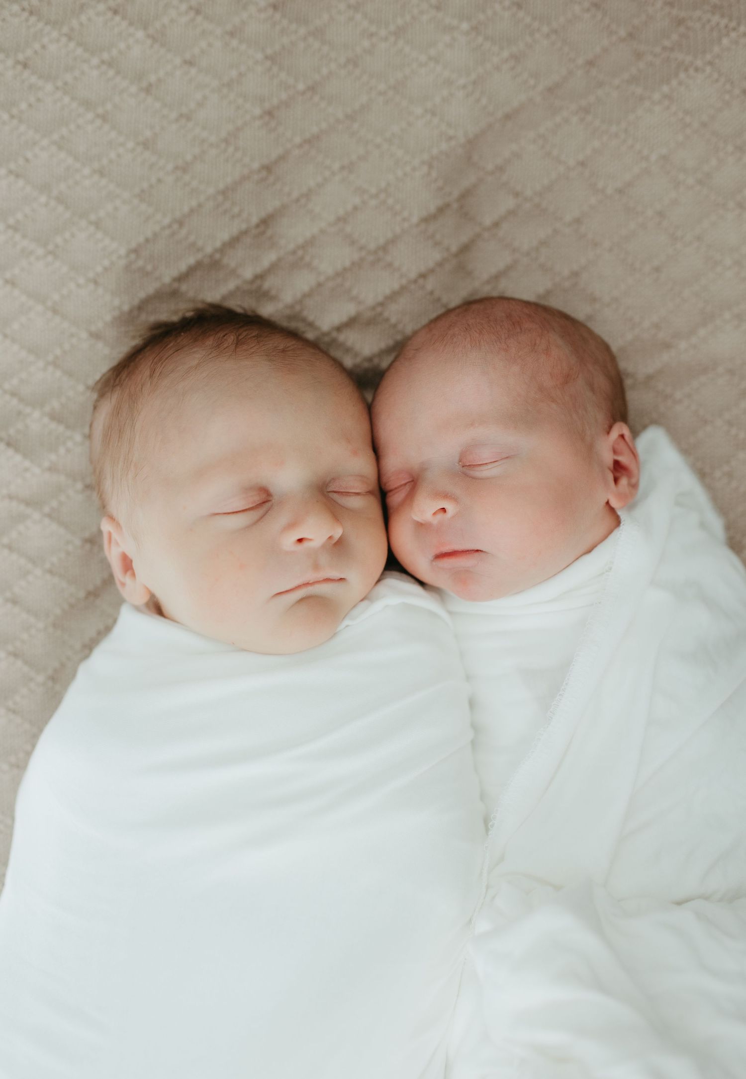 Two sleeping newborn babies lying side by side wrapped in white blankets.