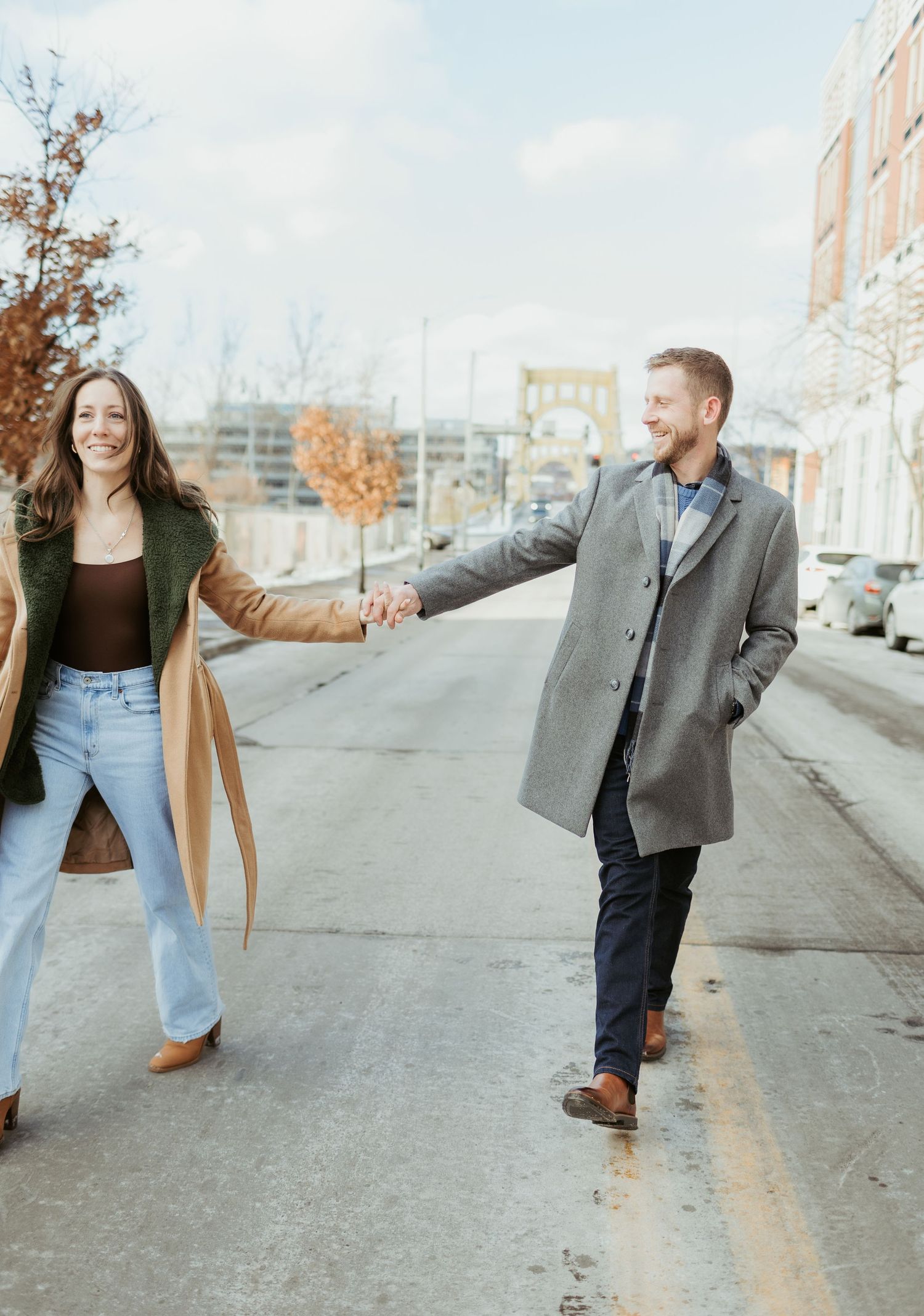 Couple holding hands while walking down a city street on an autumn day in casual winter coats.