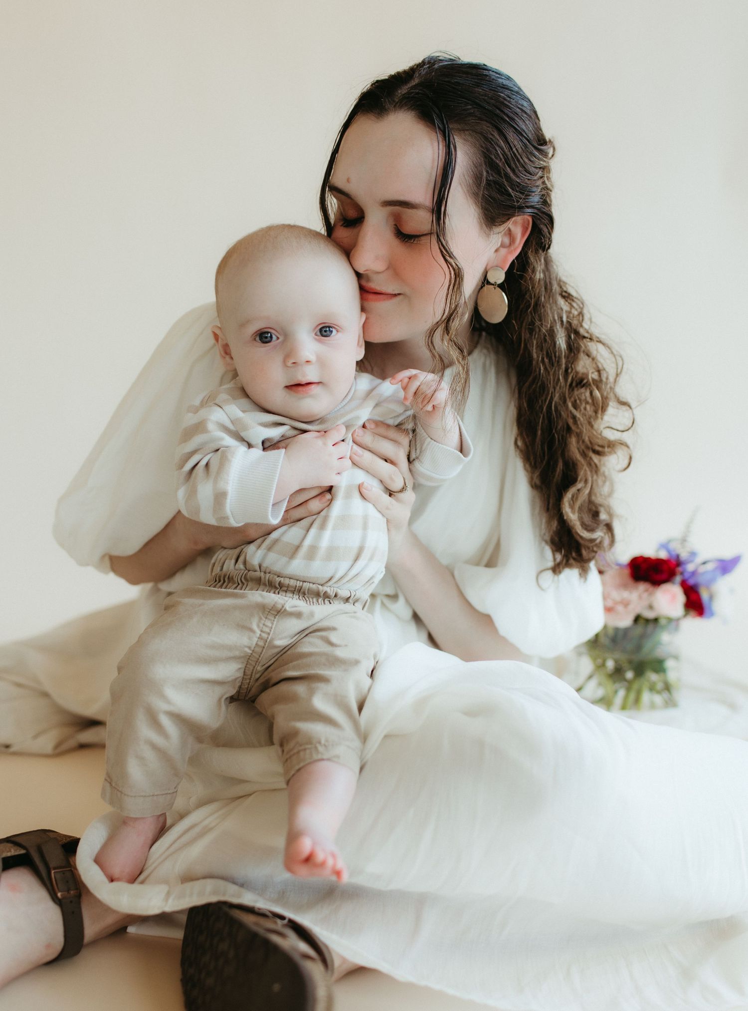 Tender moment between parent and baby in matching cream colored outfits.