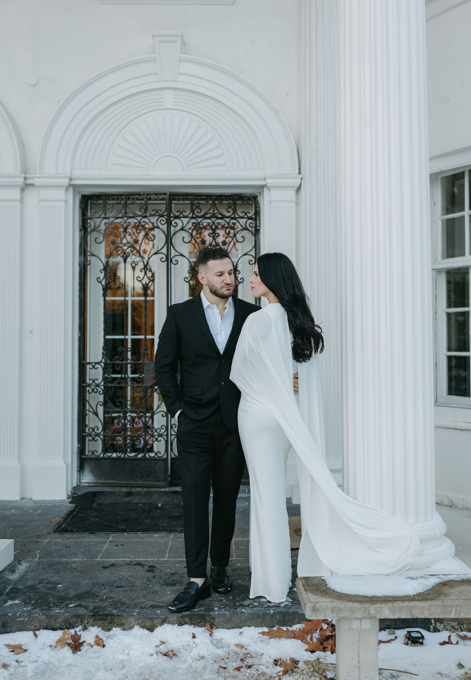 Couple in black and white formal wear posing by ornate doorway in winter.