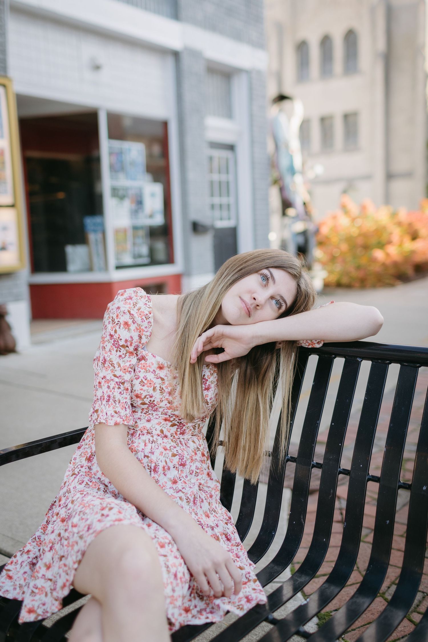 Person in floral dress resting on park bench in urban setting with autumn colors.