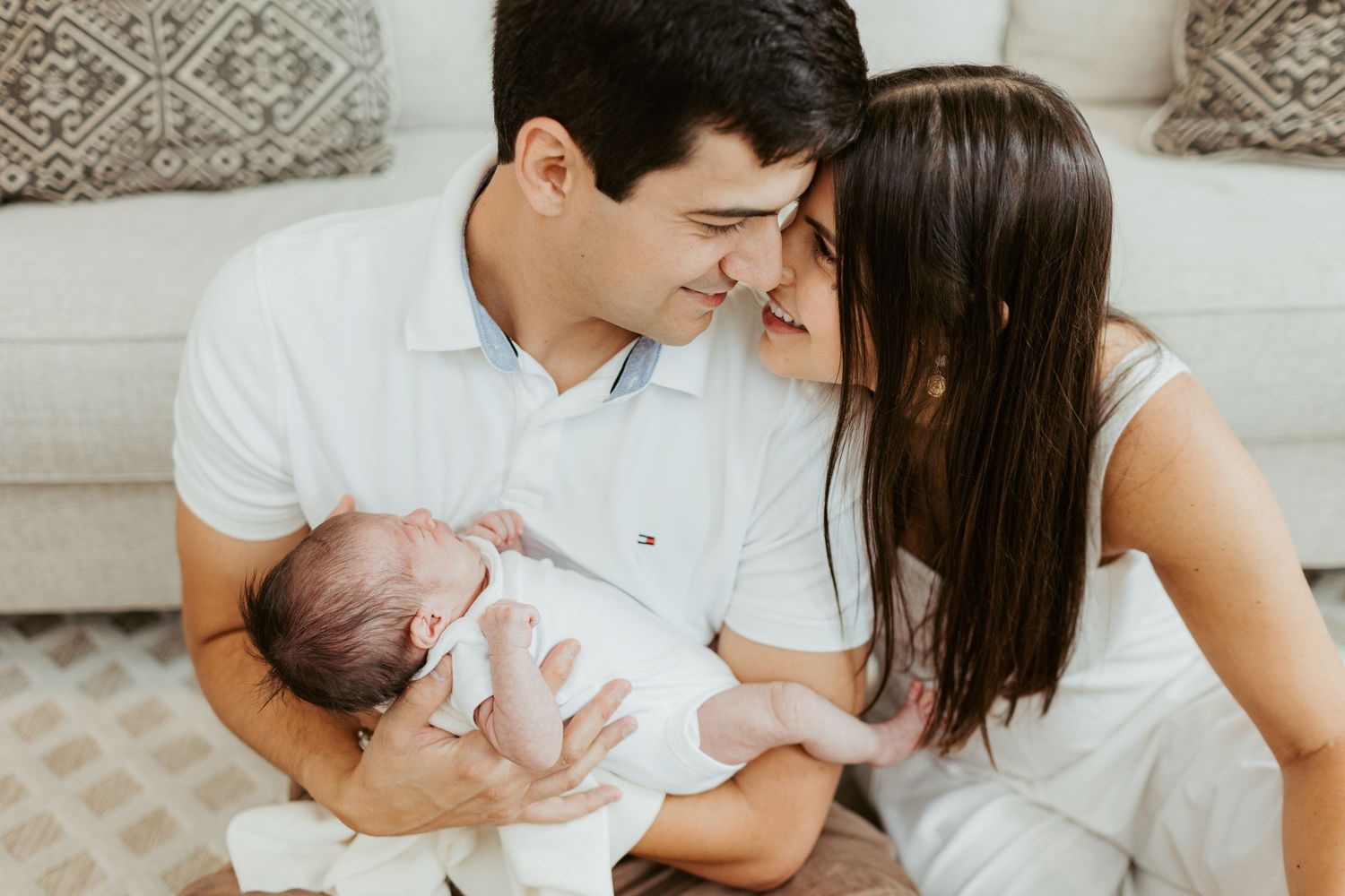 A family sharing an intimate moment while holding their newborn baby on a couch.