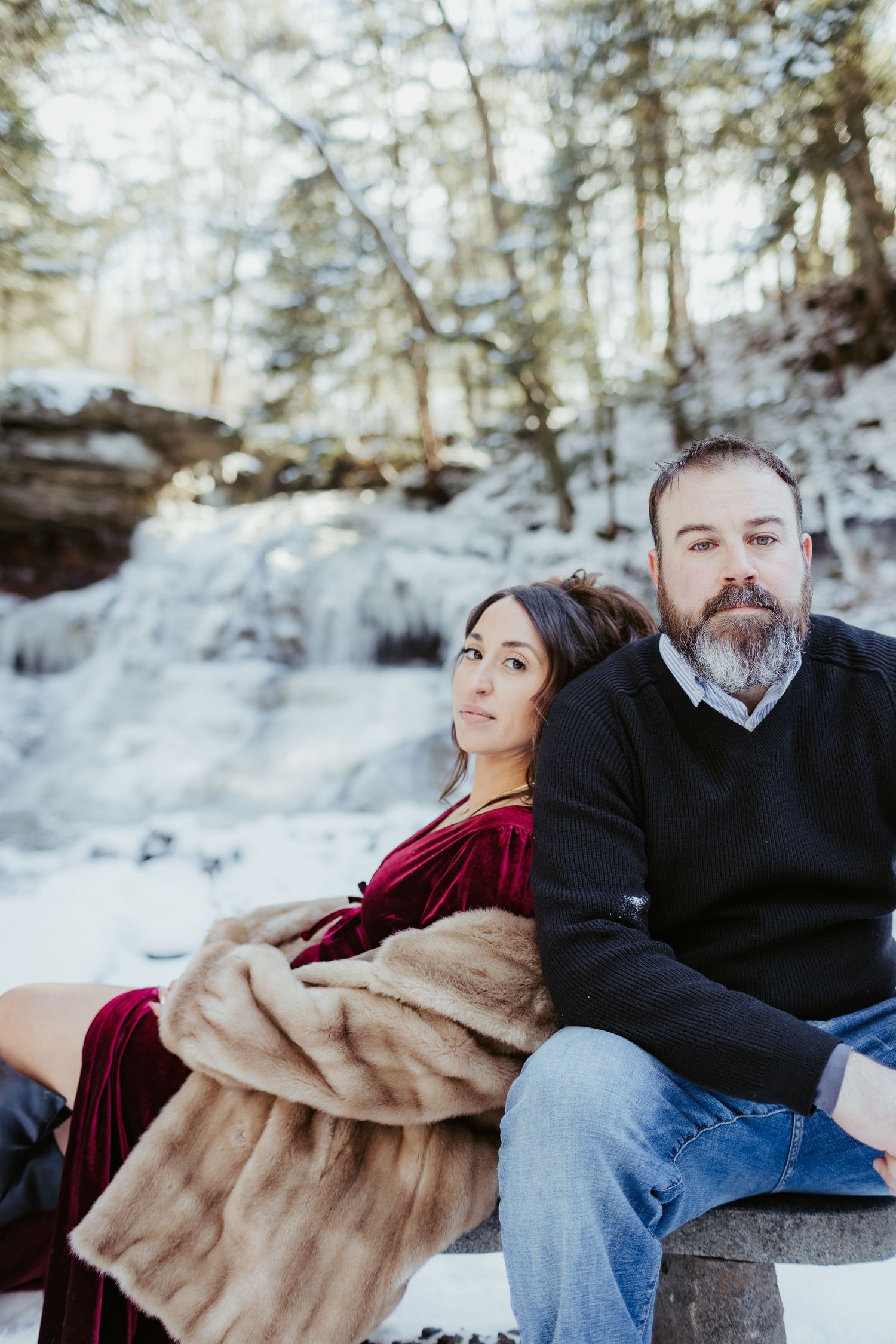 Couple sitting together near a snow-covered waterfall in winter scenery.