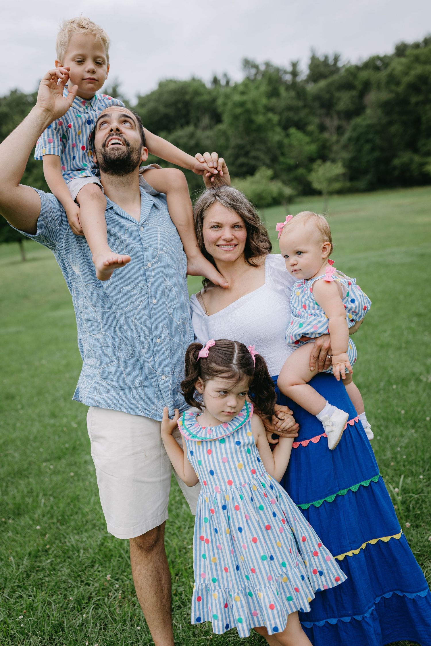 A family stands together on a grassy hill wearing coordinated blue outfits for an outdoor portrait session.