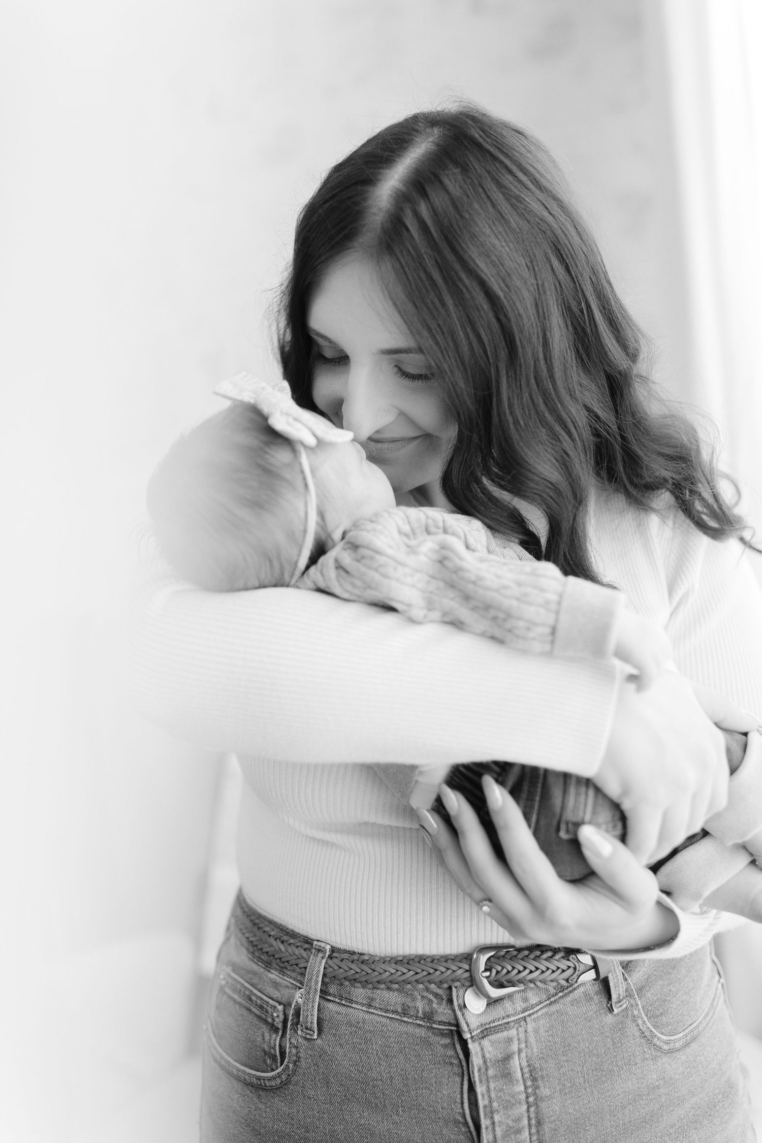 A tender black and white portrait of a mother holding and nuzzling her newborn baby.