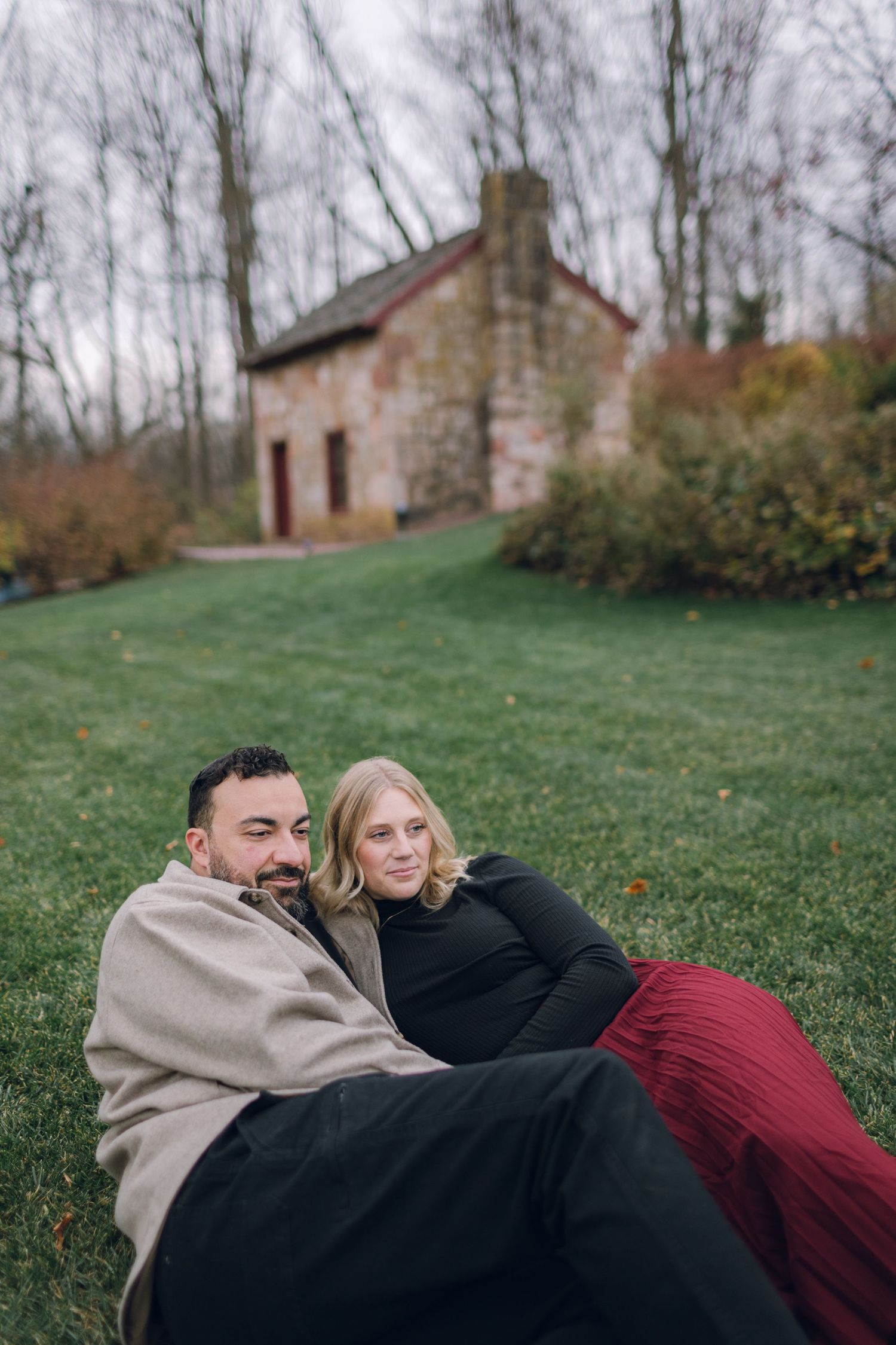 A couple relaxes on grass with a historic stone building in the background.