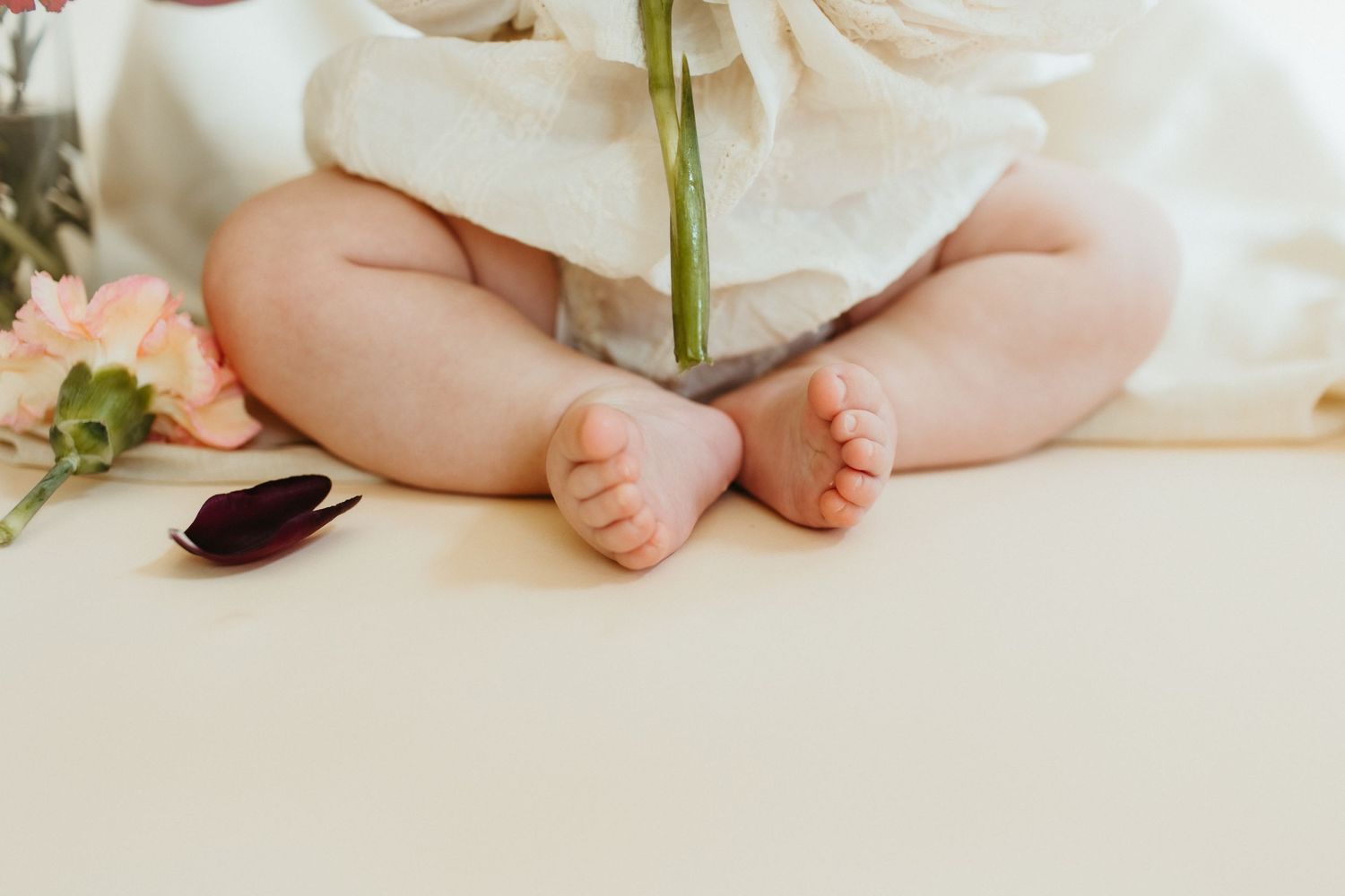 Close-up of baby's feet in white lace dress against light background.