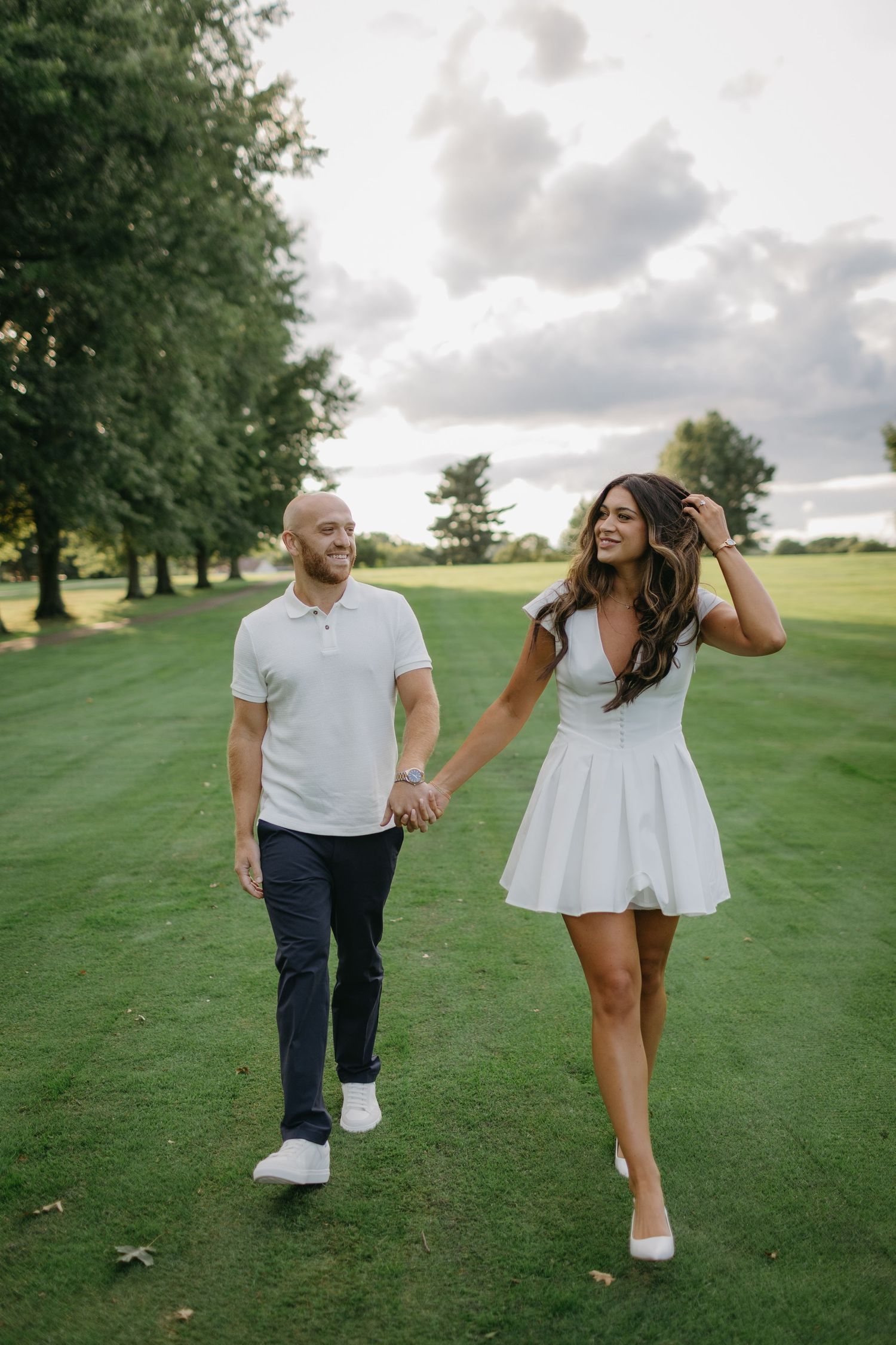 Couple walking hand in hand on a sunny golf course with white outfits.