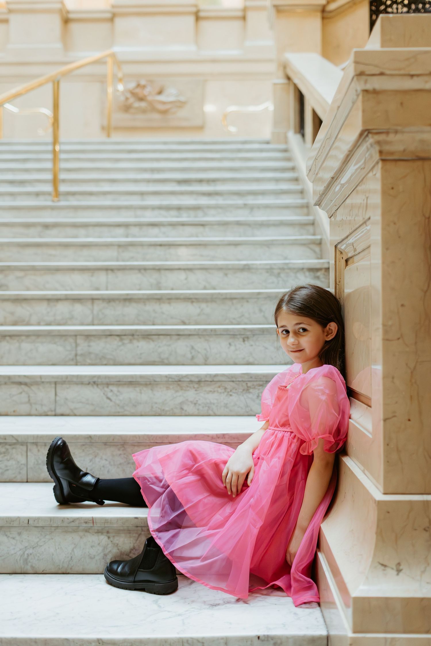 Child in pink tulle dress sitting on grand marble staircase.
