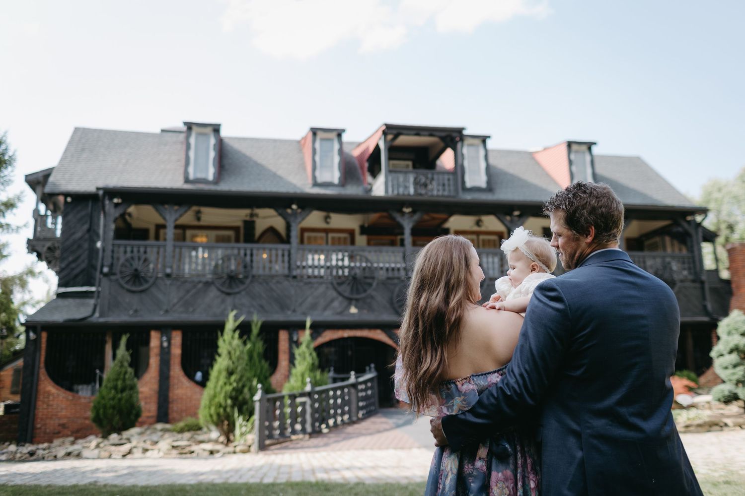 Family embraces outside dark Victorian-style building with dormer windows.
