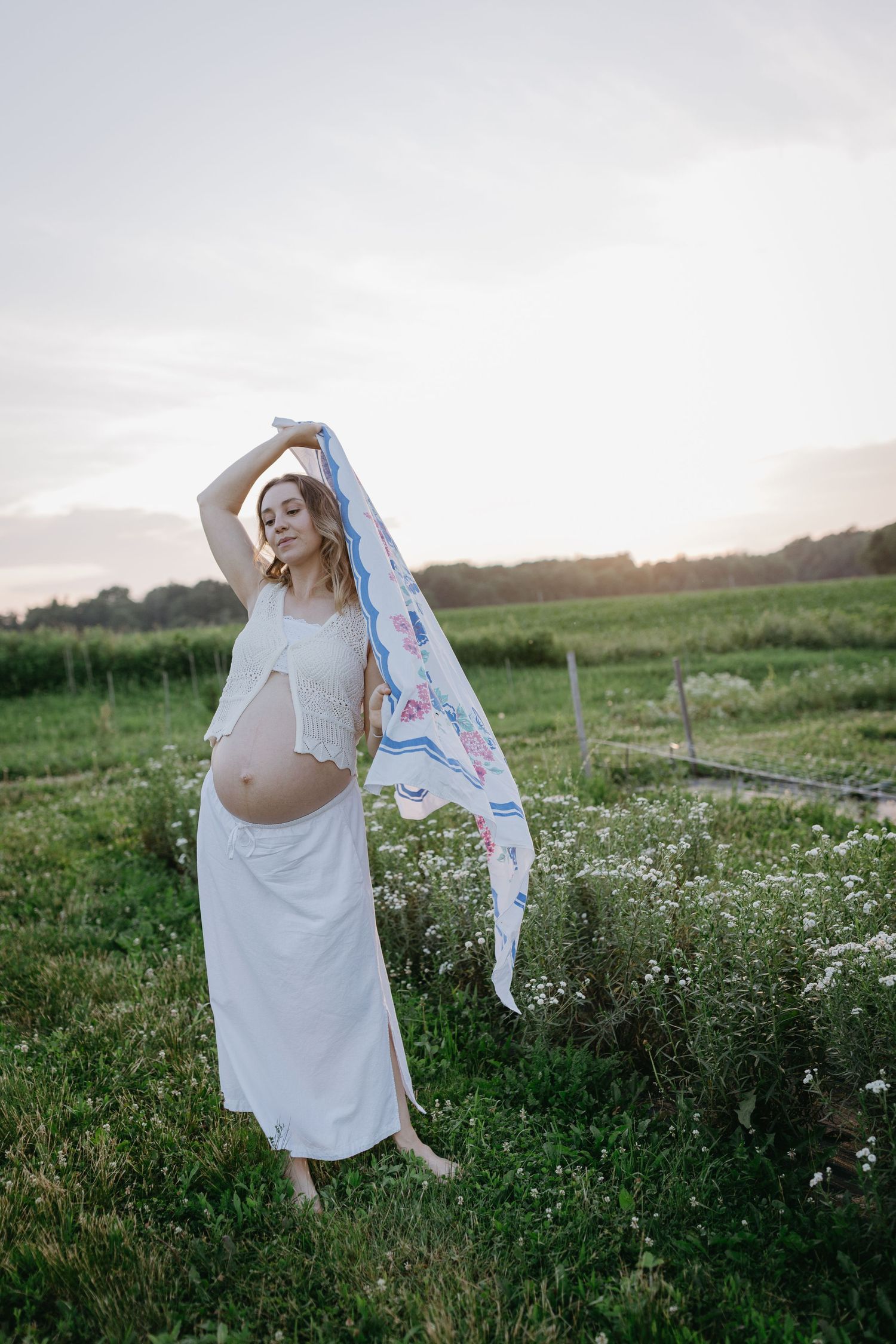 A dreamy, artistic maternity photo series of a woman in a white dress dancing in a wildflower field at sunset.