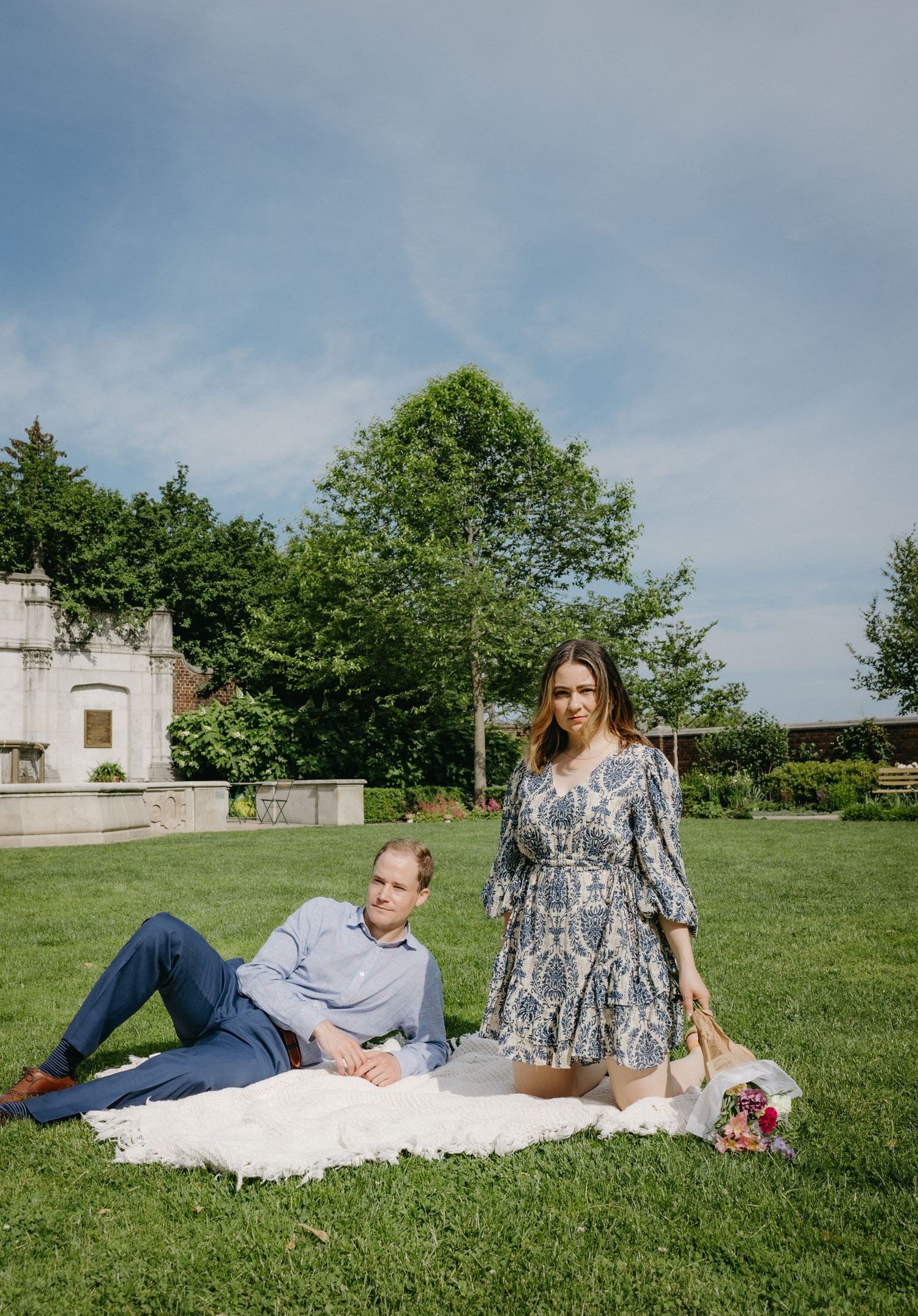 Couple relaxing on blanket with picnic spread in front of stone building.
