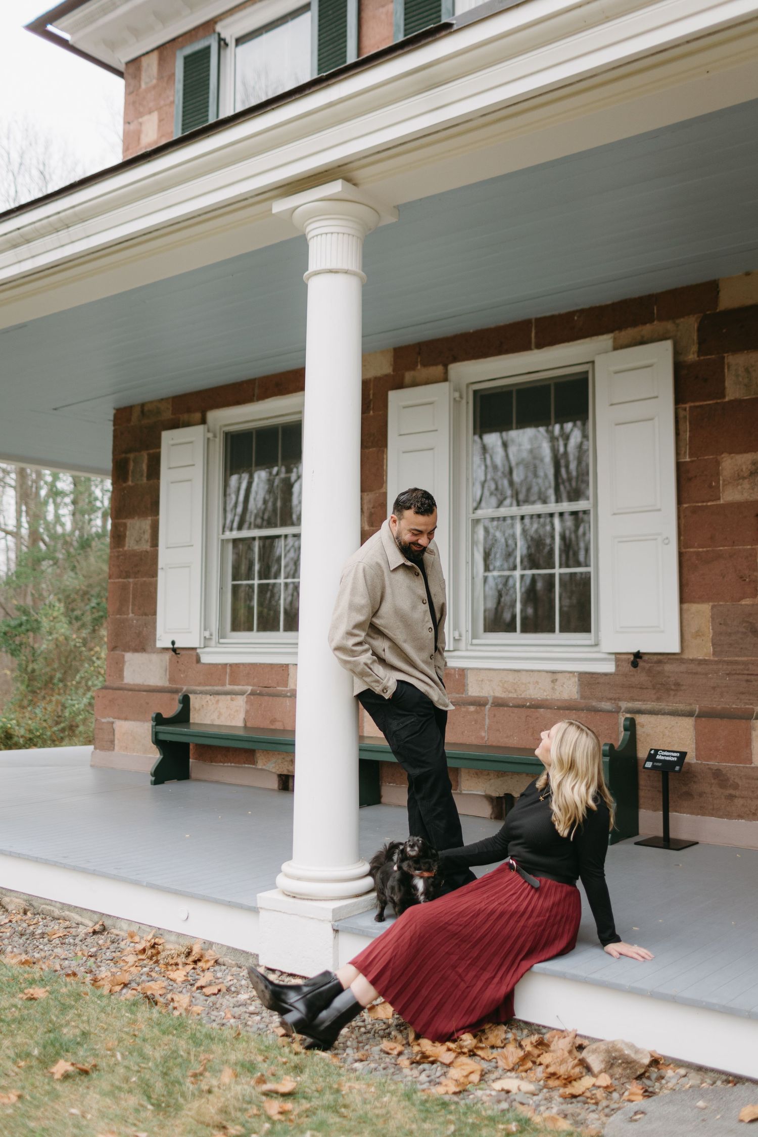 A couple shares a moment on a colonial-style porch with white columns and brick walls.