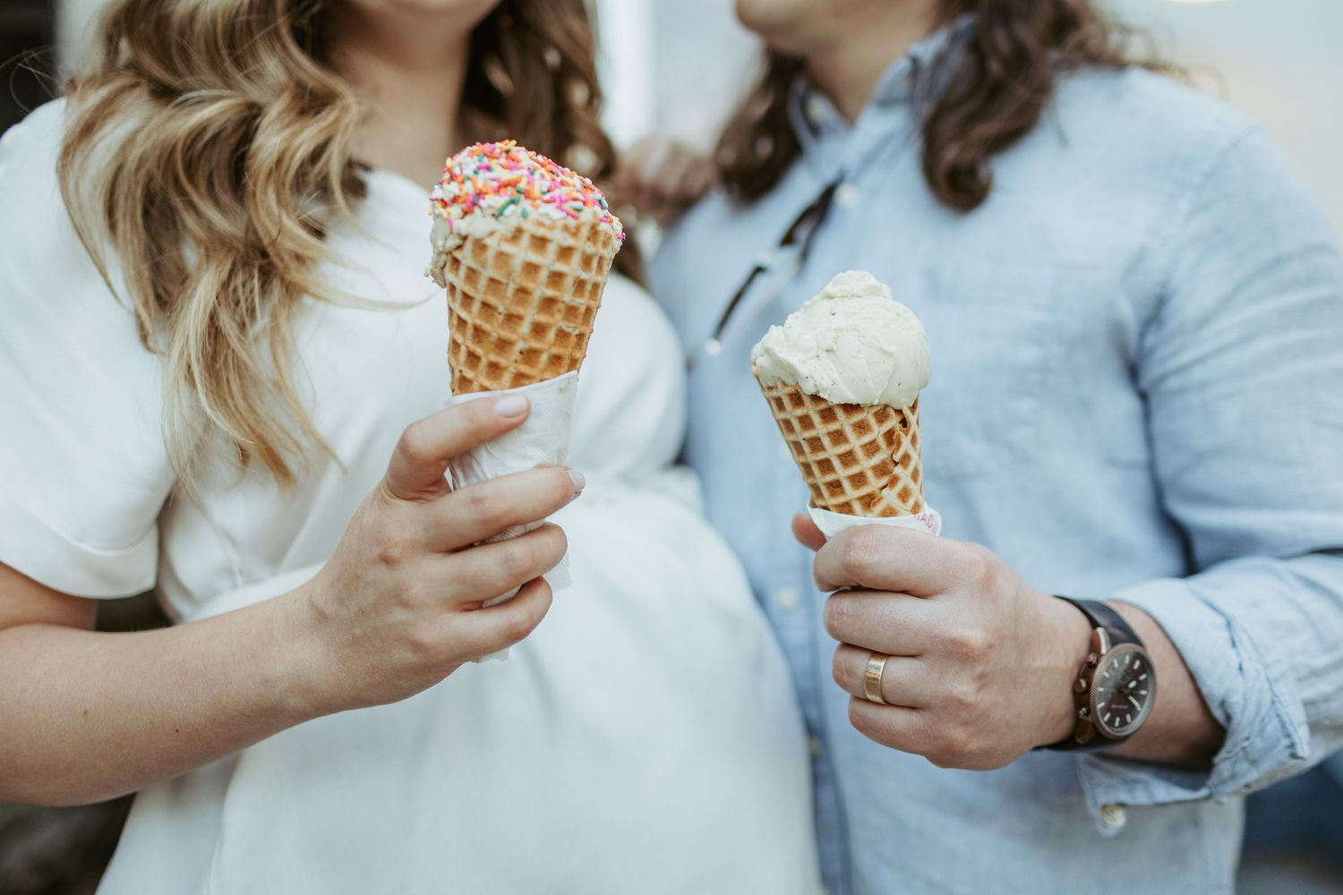 Two hands holding ice cream cones with sprinkles against a blurred background.
