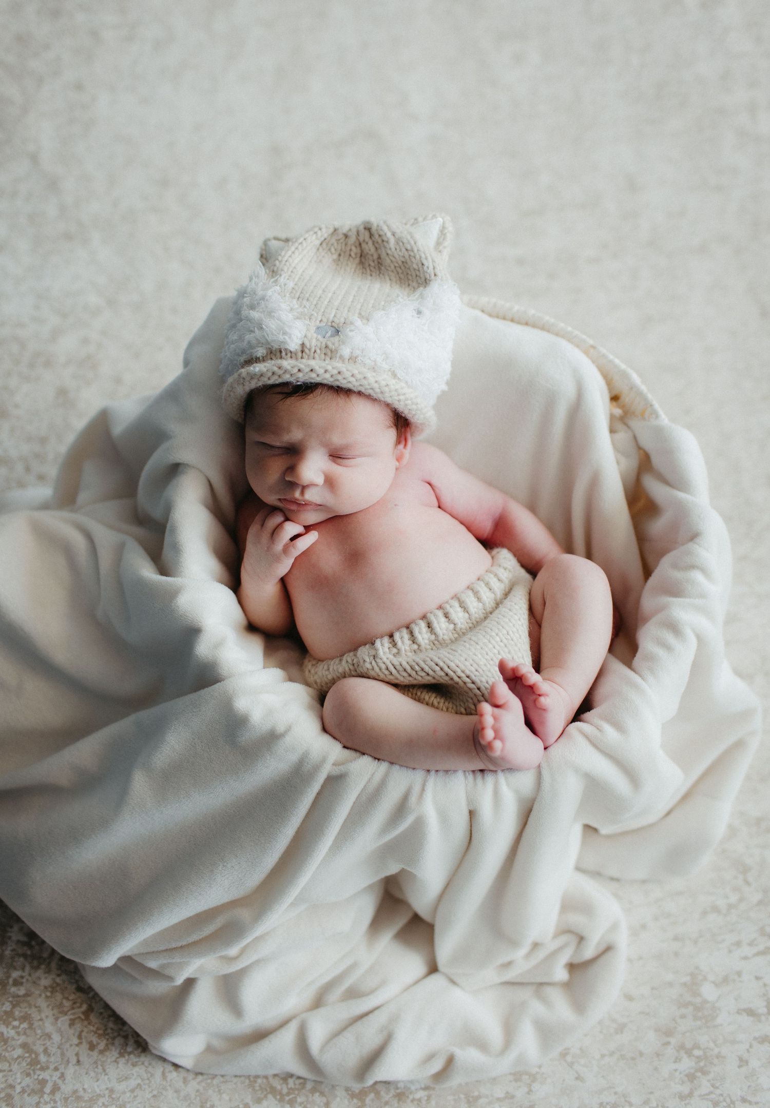 Sleeping newborn wearing knit cat hat wrapped in soft cream blanket.