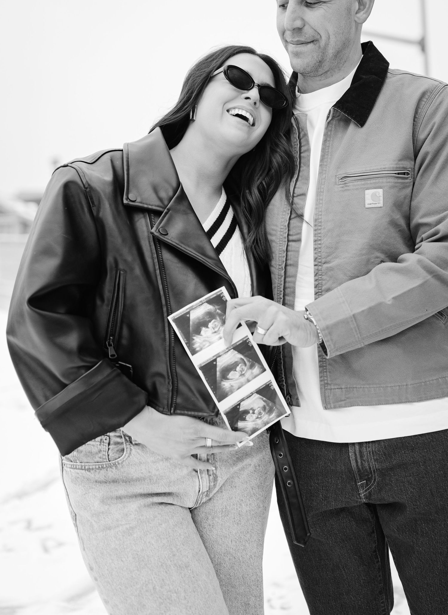 A joyful black and white photo of a couple sharing their ultrasound images.