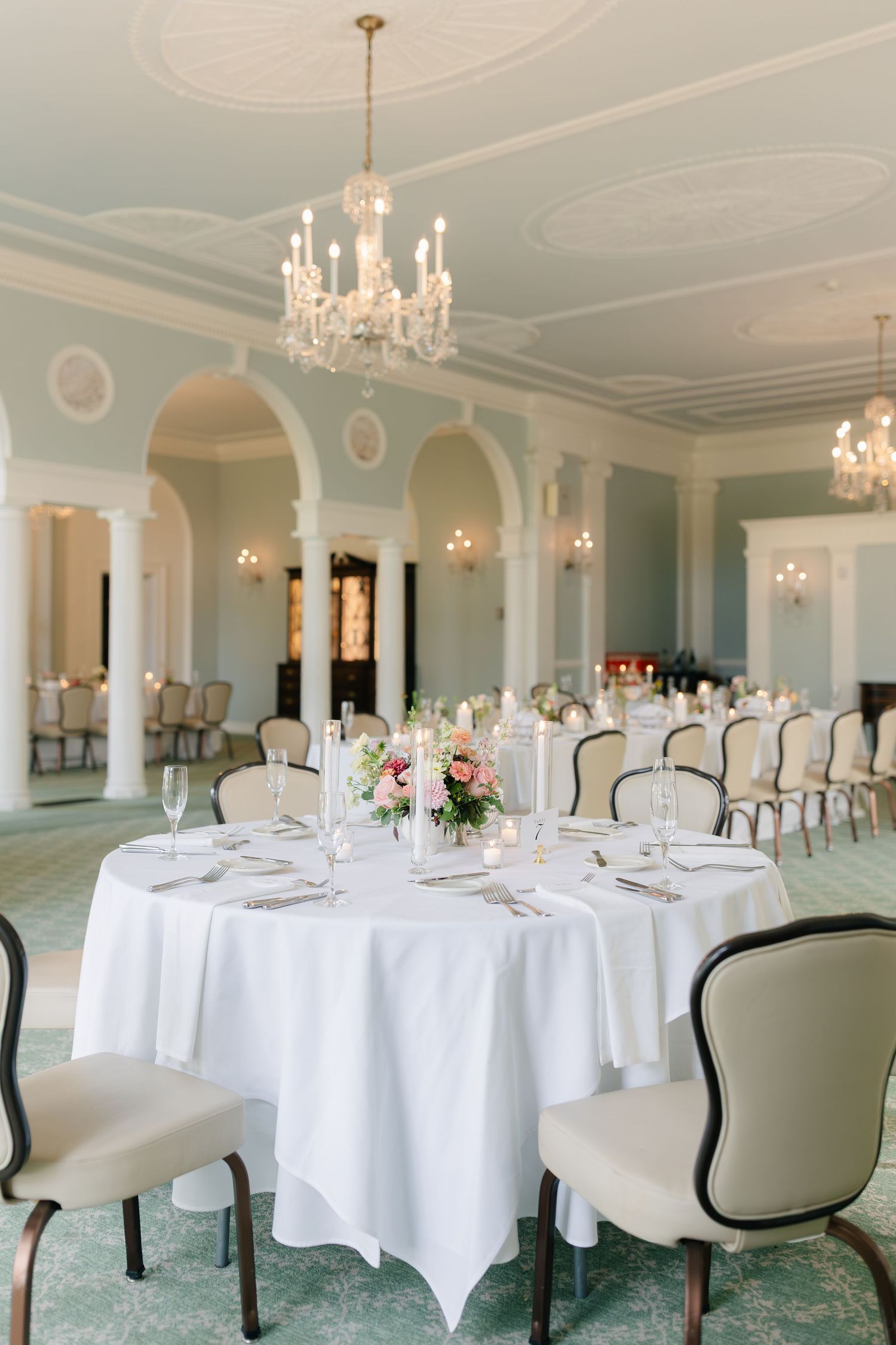 Elegant ballroom with crystal chandeliers, round tables with white linens, and mint green carpeting set for formal dining.