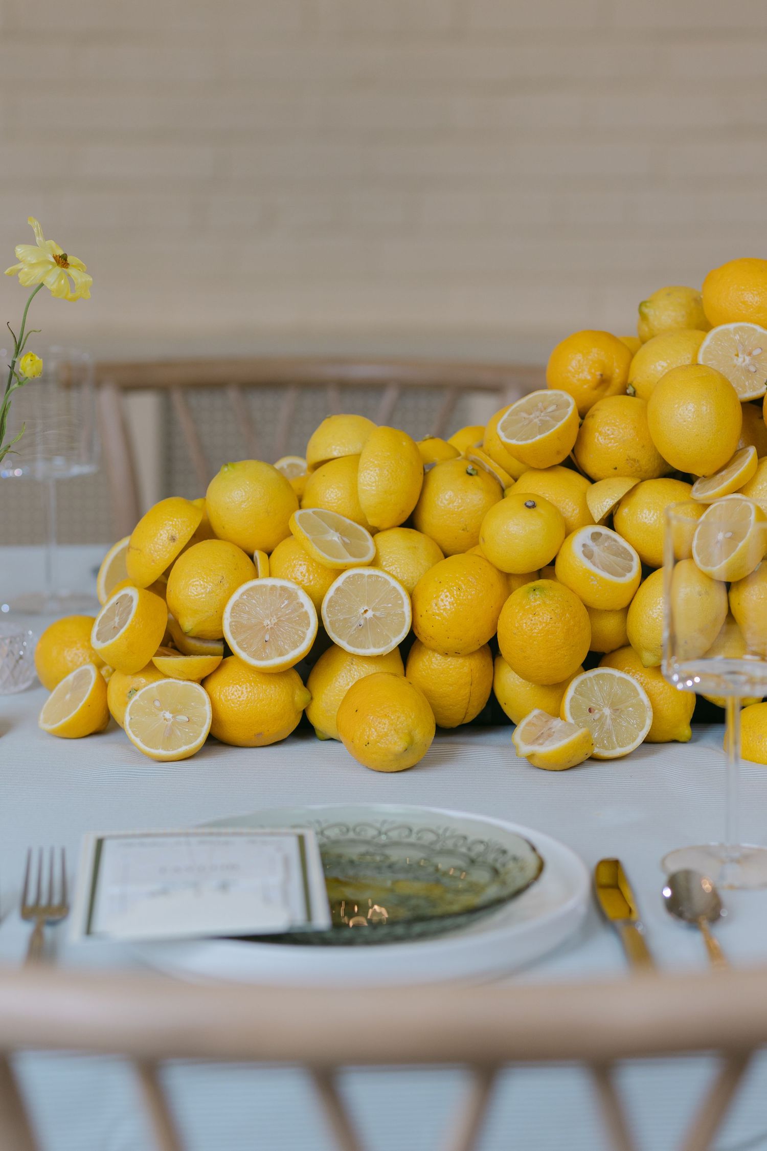 Elegant table centerpiece featuring a large pile of fresh yellow lemons, some halved, with place settings and gold cutlery.