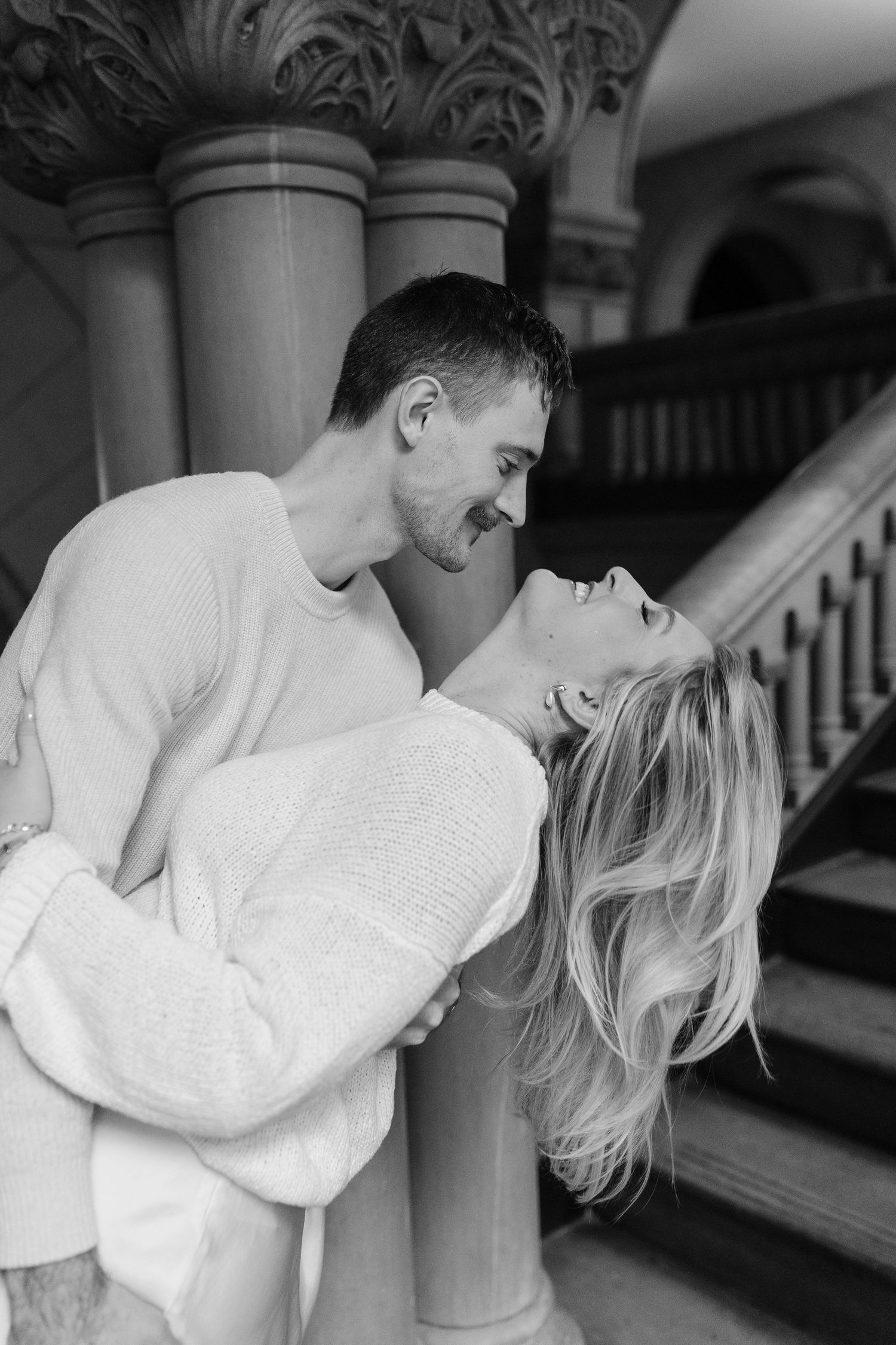 A romantic black and white photo series showing a couple in white clothing embracing near ornate columns.