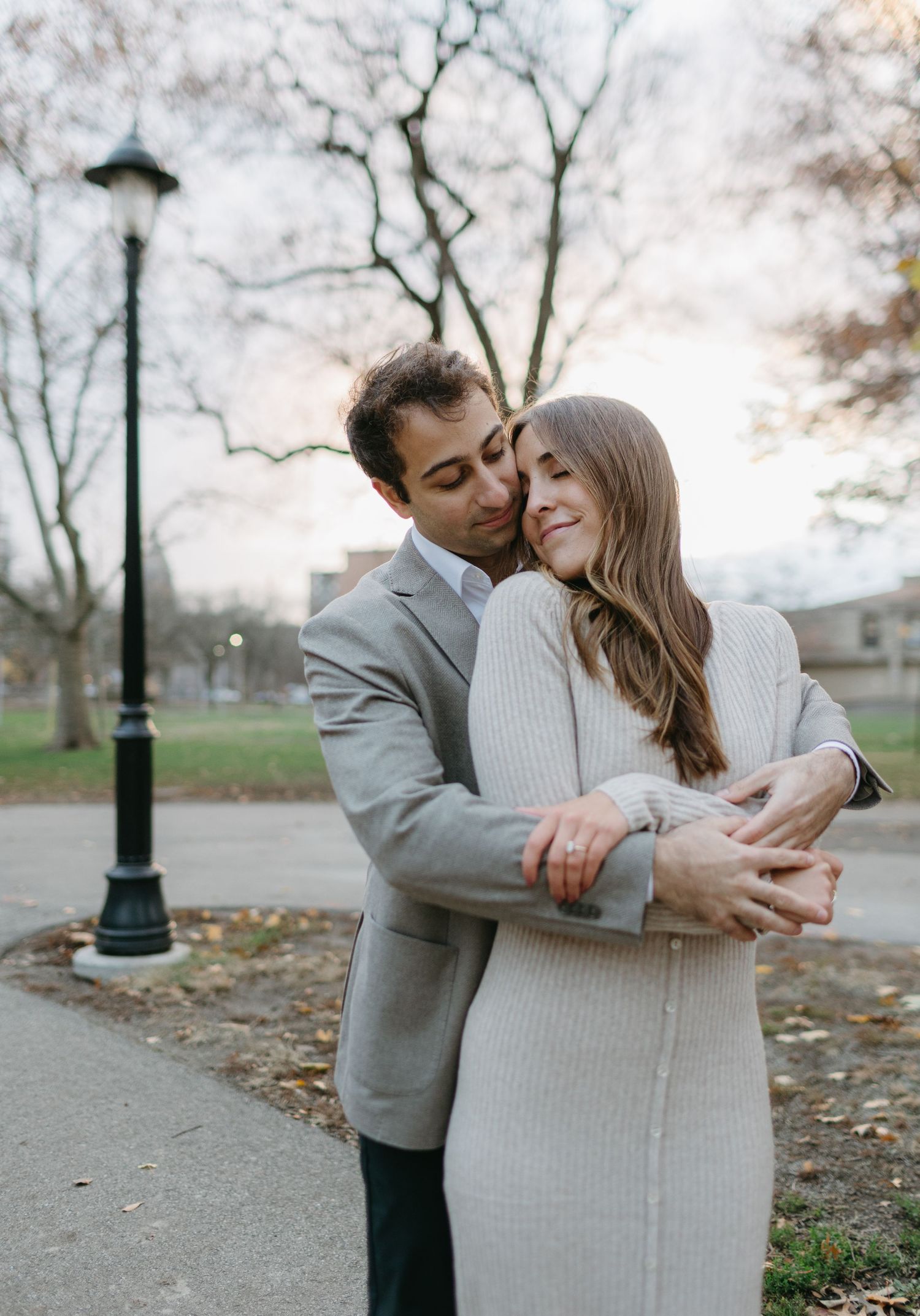 A romantic embrace captured in a park with a street lamp and bare trees in the background.