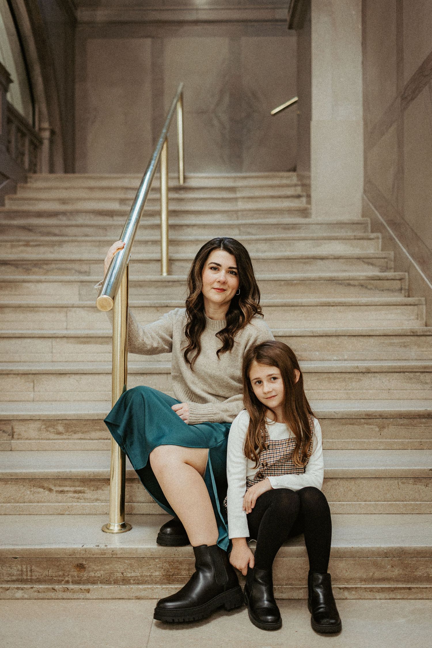 Two people sitting on marble staircase wearing coordinated winter outfits and boots.