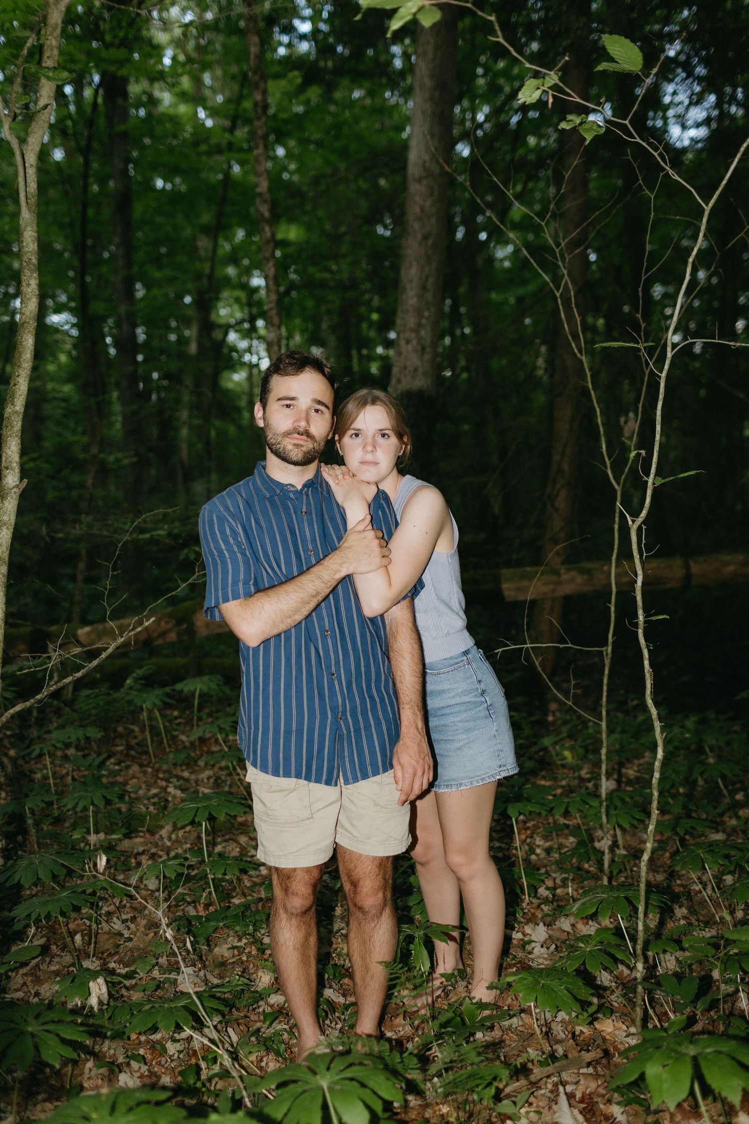 Couple embracing in forest setting wearing casual summer attire.