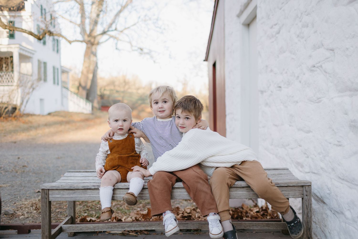 Children sitting together on wooden bench outside rustic building.