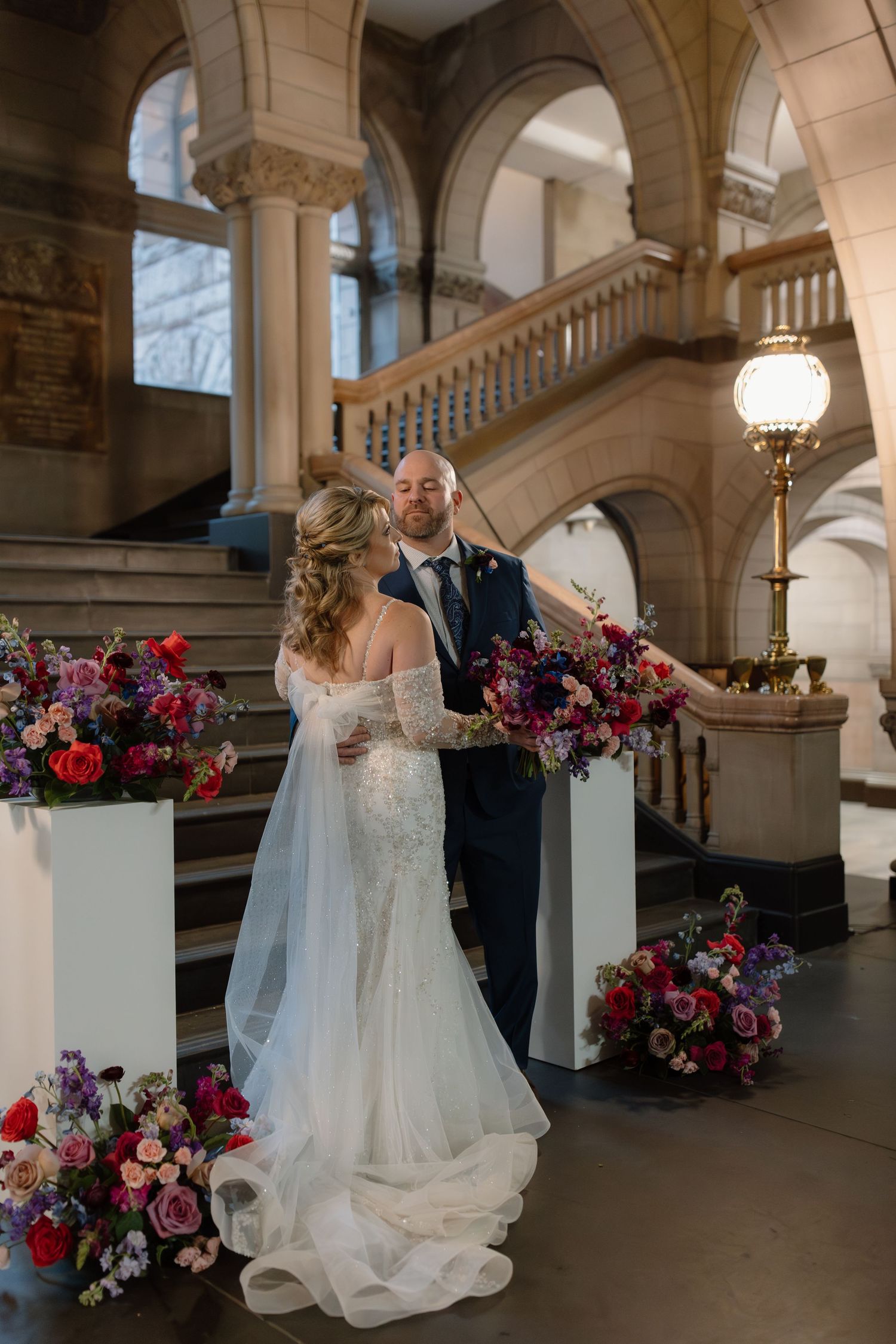A romantic wedding photoshoot sequence in an elegant stone archway corridor with vibrant red and purple floral arrangements.
