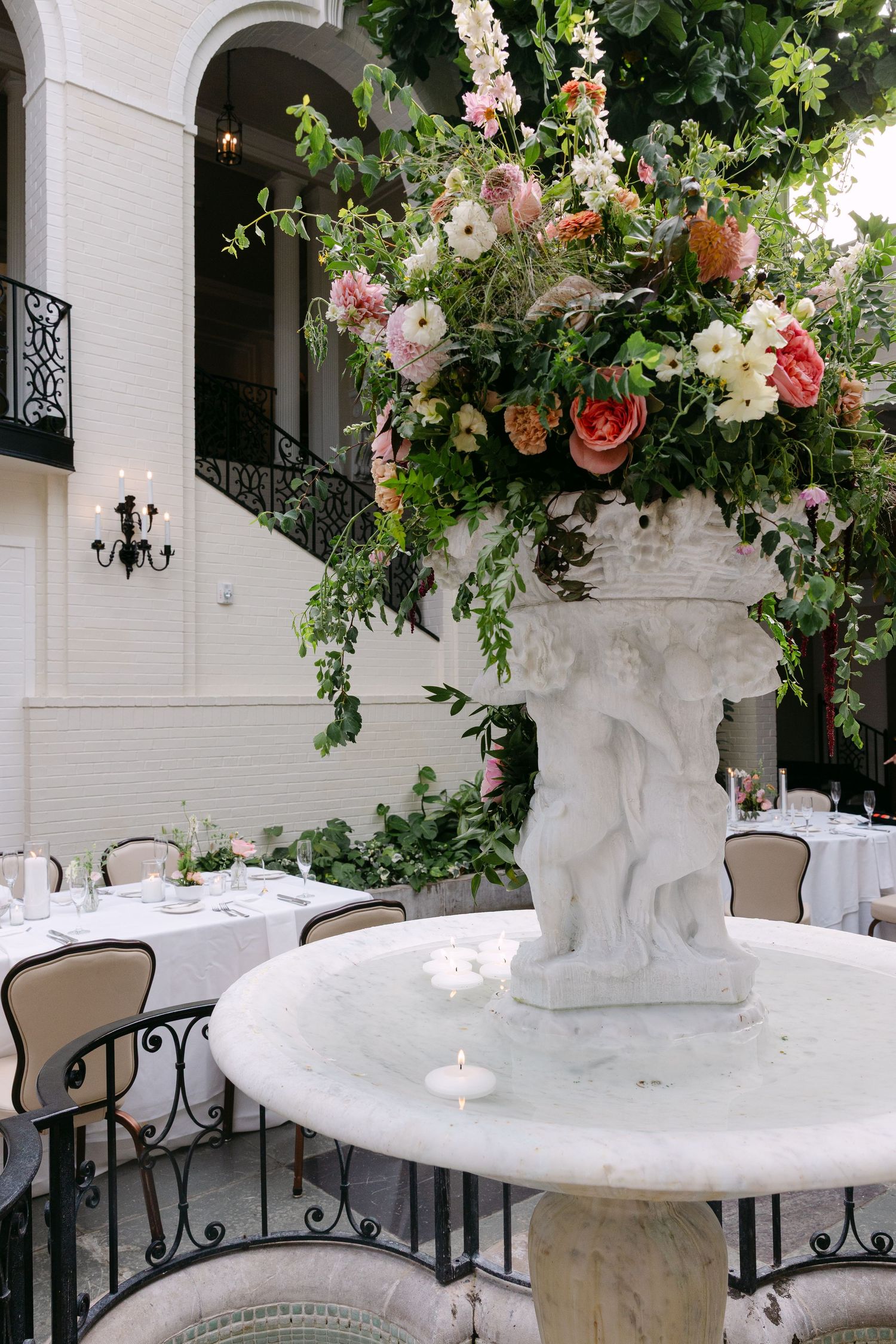 Elegant white marble fountain pedestals decorated with cascading pink and white floral arrangements at a wedding venue.