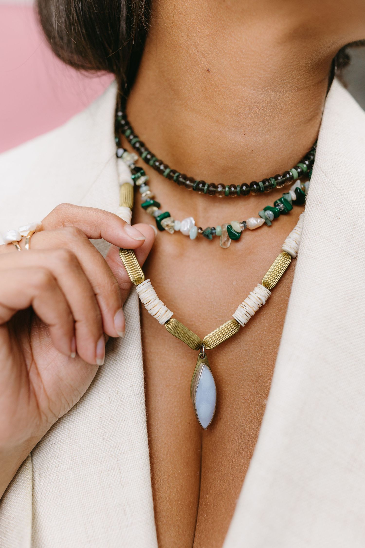 Close-up of layered beaded necklaces featuring turquoise stones, white shell beads and a white pendant on tanned skin.