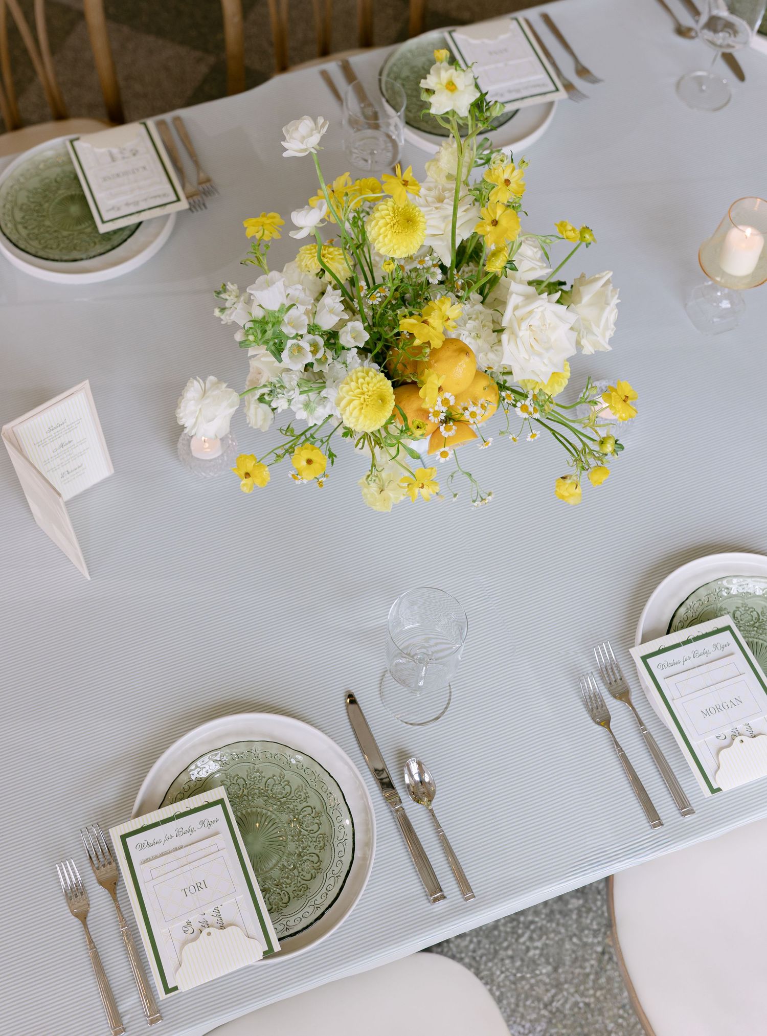 Elegant wedding table setting with yellow and white floral centerpiece, green plates, and silver cutlery on a white tablecloth.