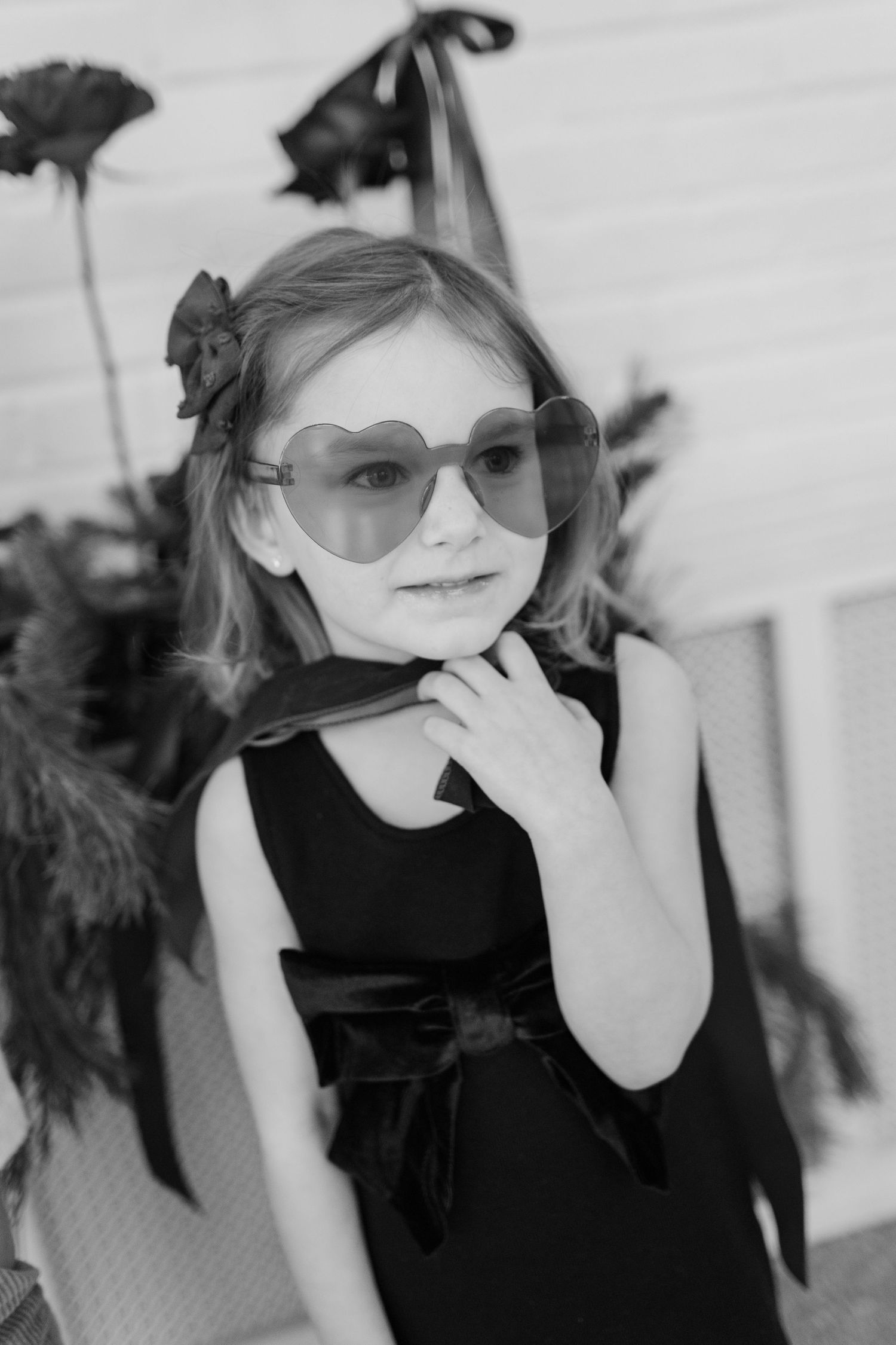 Young girl in black dress and aviator sunglasses poses stylishly in black and white portrait.